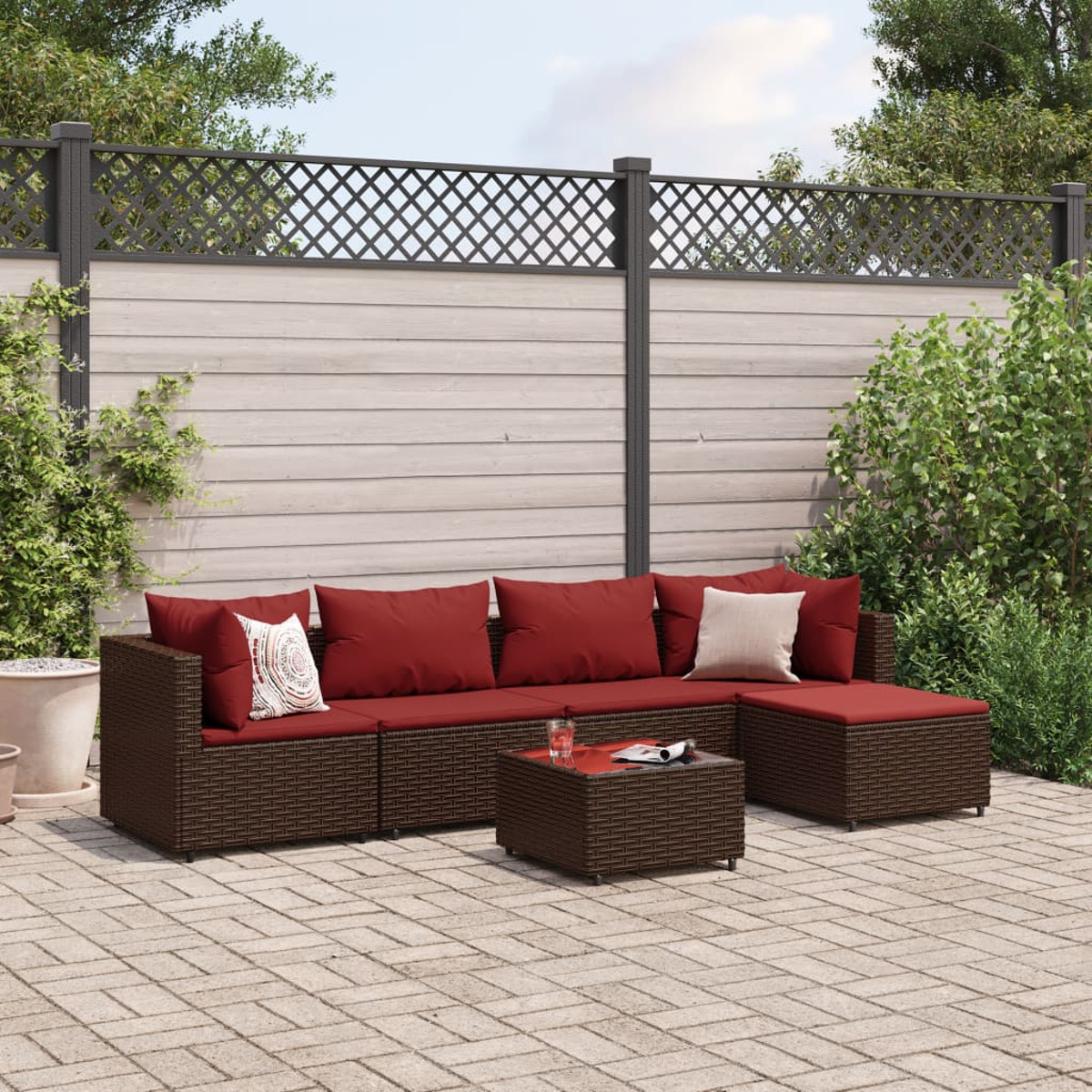 Outdoor-Ecksofa in braunem Korbgeflecht mit roten Kissen, Couchtisch und Pflanzen.