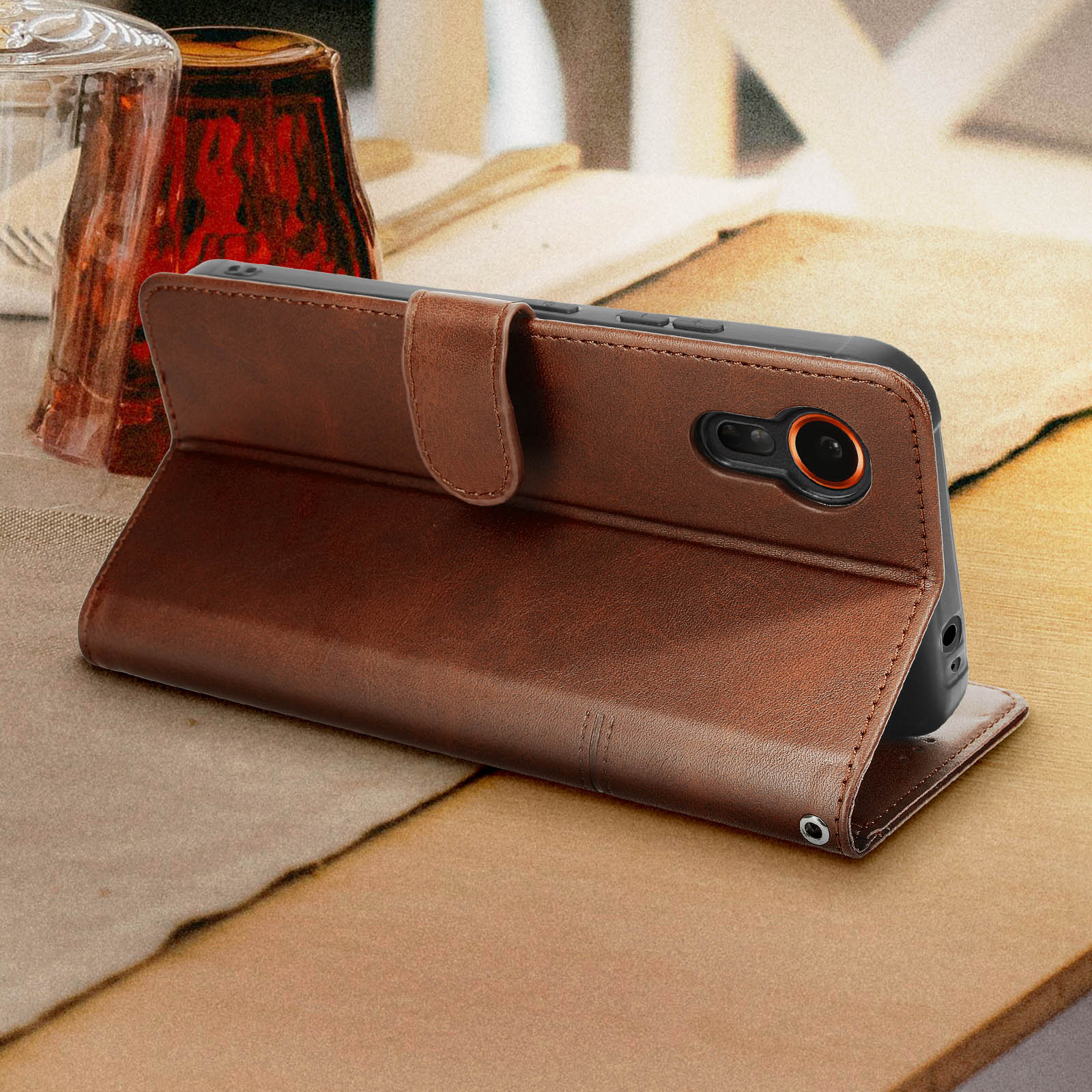 Eine braune Handyhülle, die aufrecht steht, mit einem Telefon darin, auf einem Tisch.