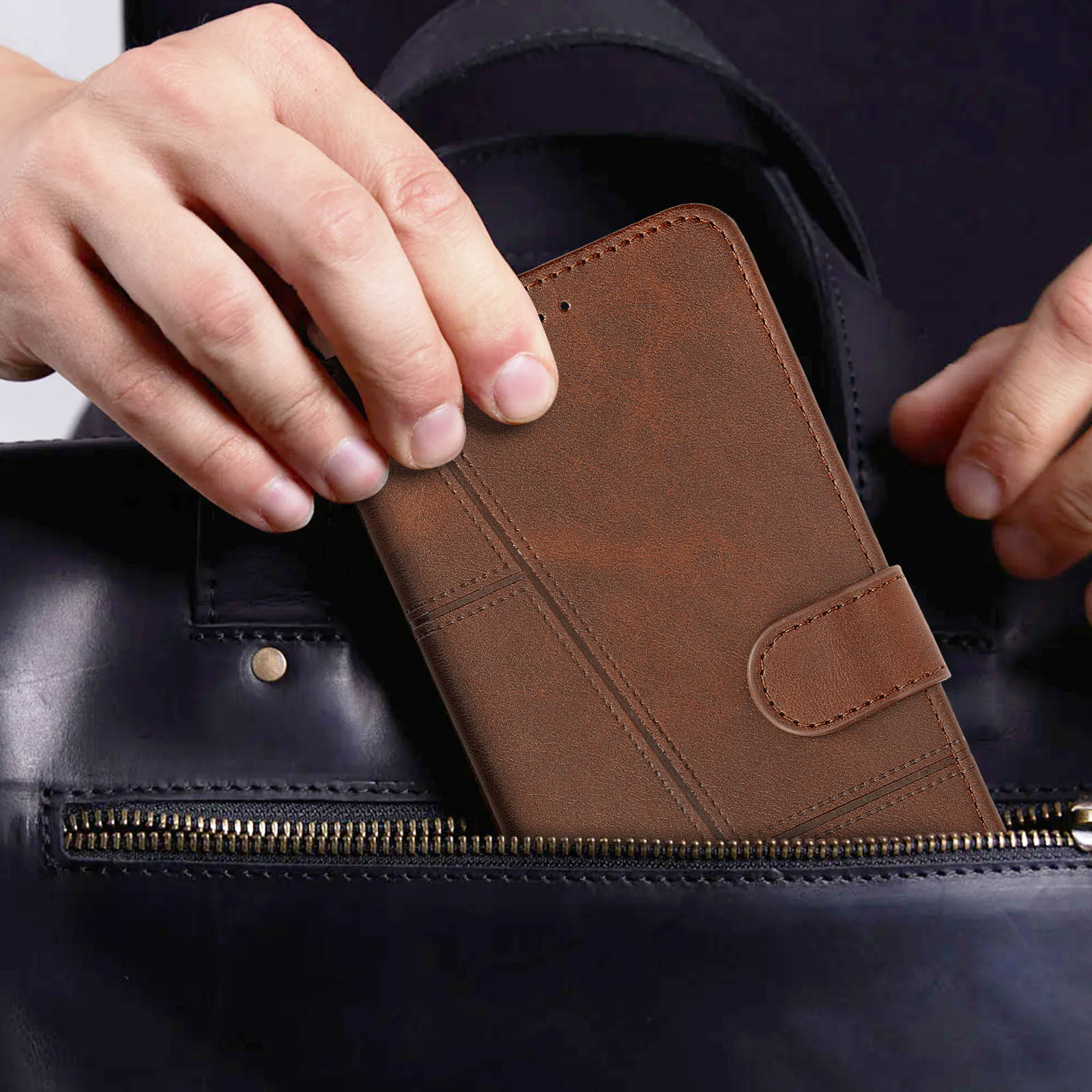 Eine Hand legt eine braune Leder-Handyhülle in eine schwarze Ledertasche. Die Tasche ist geöffnet.