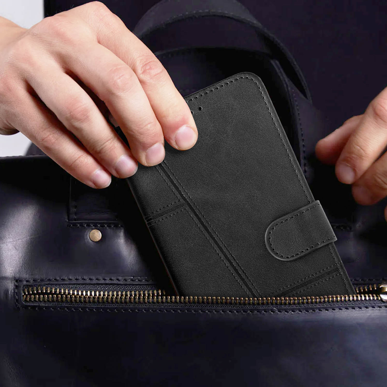 Hände, die eine schwarze Handyhülle in eine dunkelblaue Ledertasche mit Reißverschluss legen.