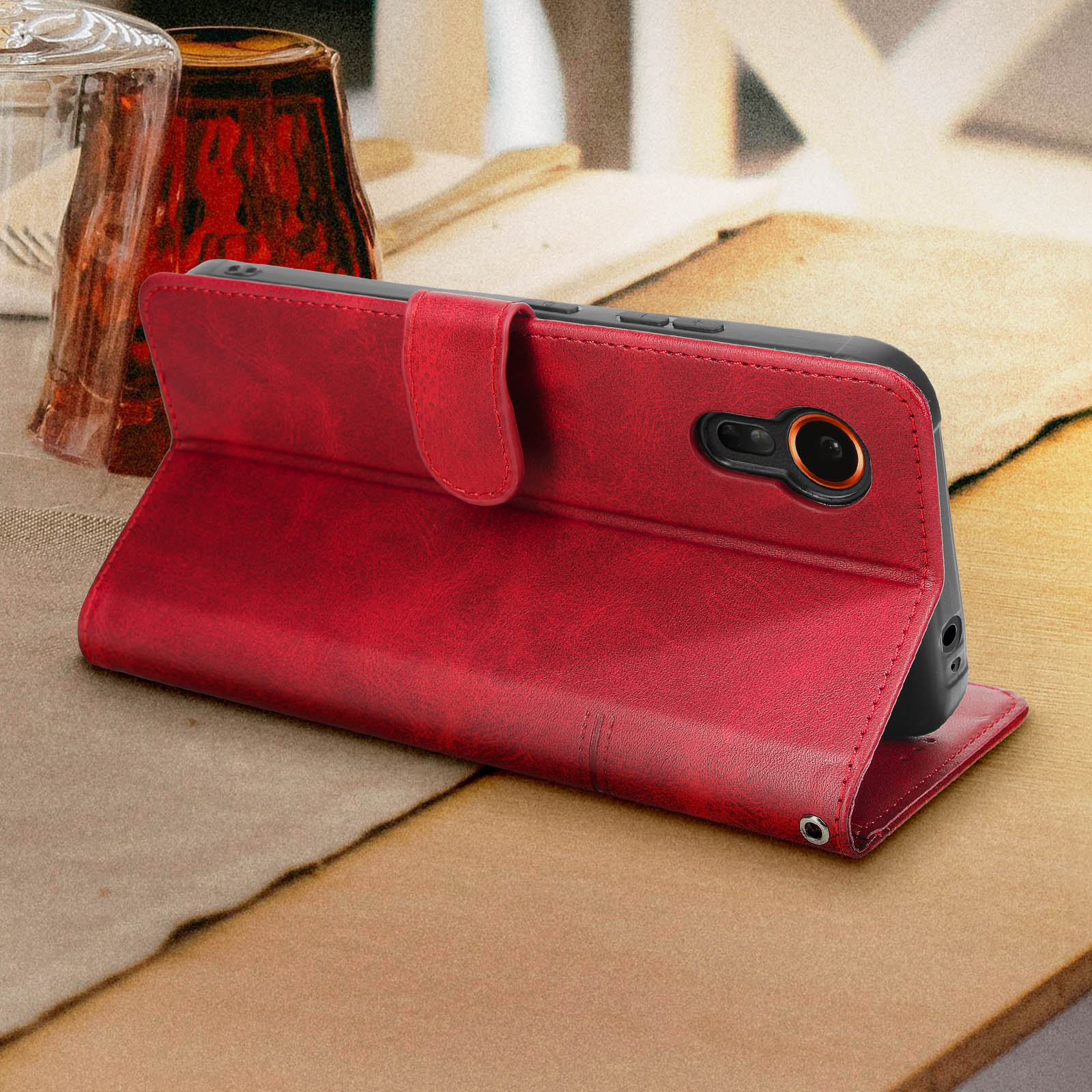 Rote Leder-Handyhülle, offen, mit Telefon. Auf hellbraunem Tisch, mit Glas und Papier.