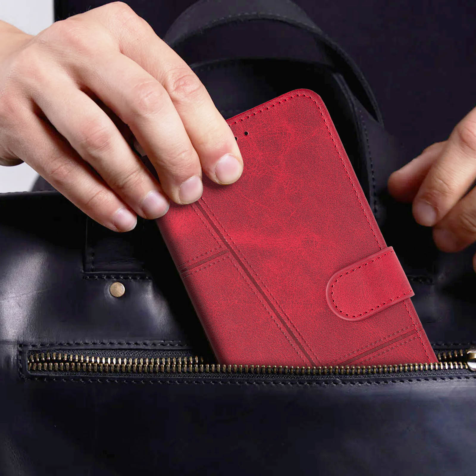 Hand legt rote Handyhülle in eine schwarze Ledertasche. Die Hülle ist geschlossen.