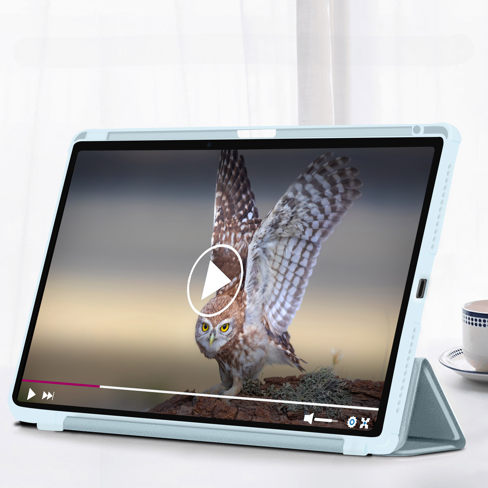 Tablet in una custodia azzurra che riproduce un video di un gufo. Una tazza è accanto.
