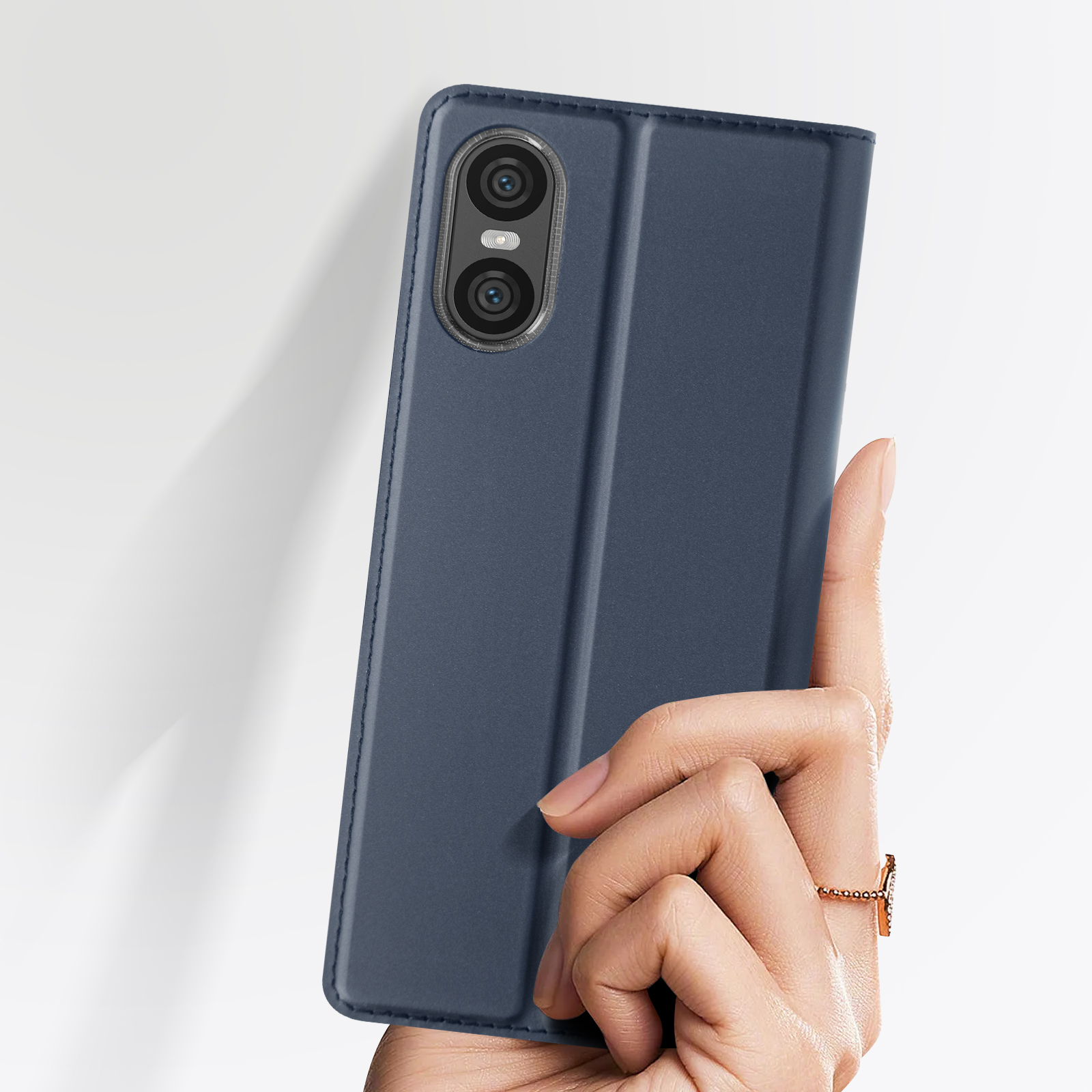 Étui de téléphone bleu foncé, partiellement ouvert, tenu par une main. Deux objectifs de caméra sont visibles.
