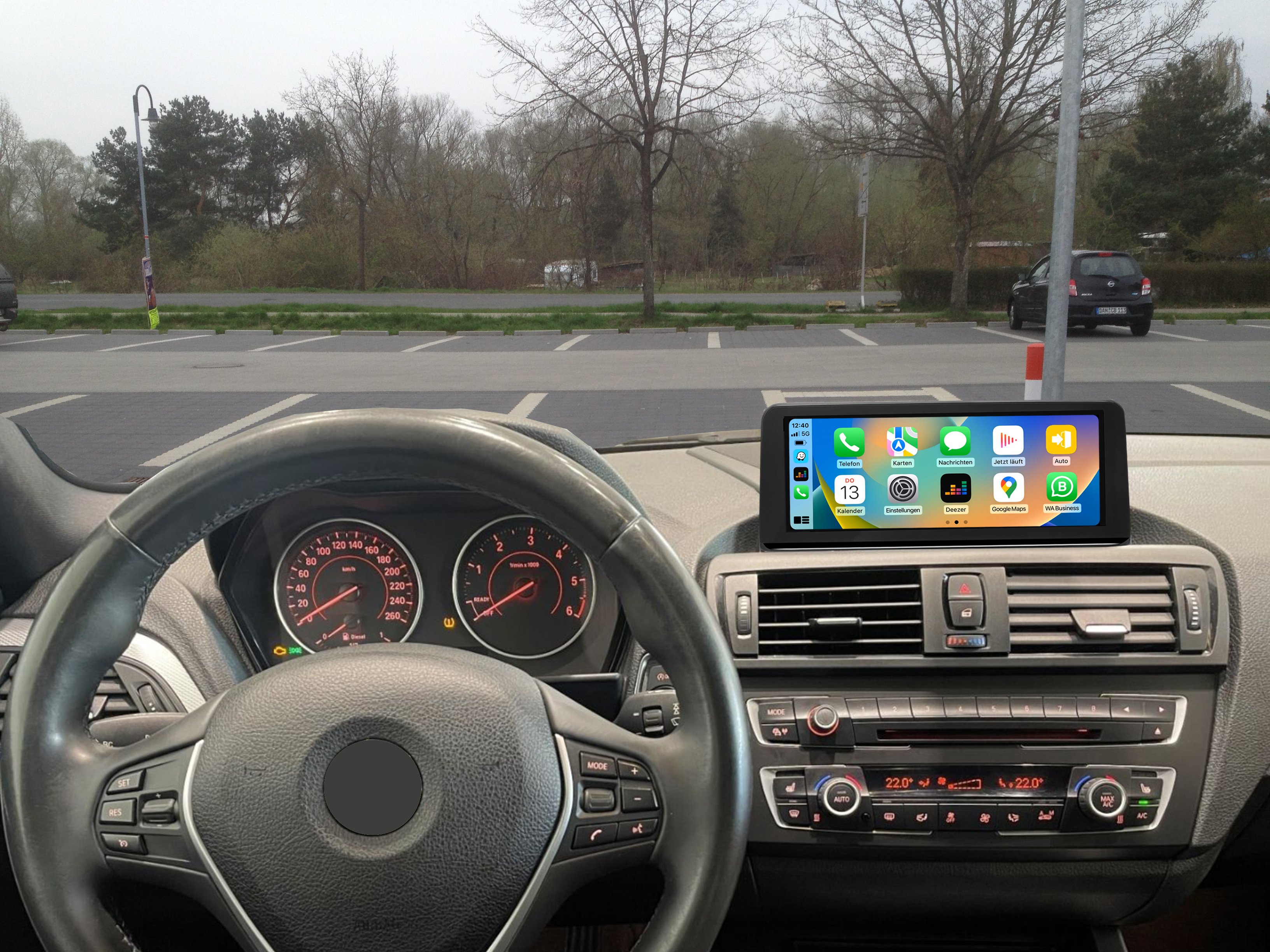 Auto-Armaturenbrett mit Bildschirm, der App-Symbole zeigt, Parkplatz draußen sichtbar.