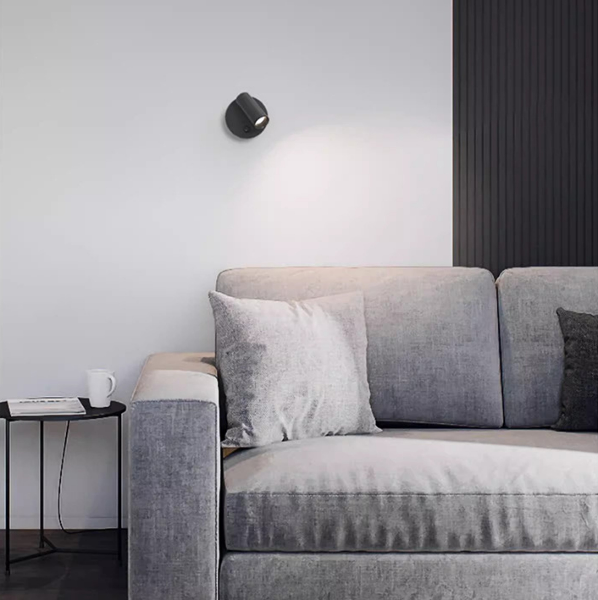 Modernes Wohnzimmer mit grauem Sofa, schwarzem Beistelltisch und Wandleuchte.