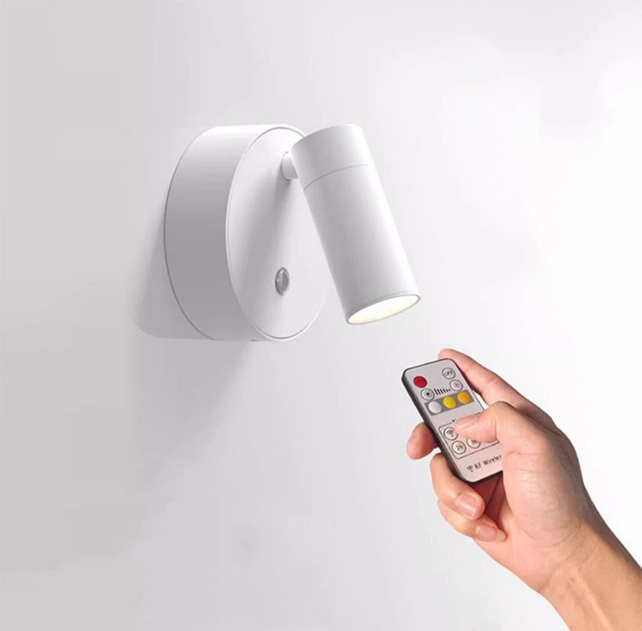 Weiße Wandleuchte mit Richtkopf. Eine Hand hält eine Fernbedienung, um das Licht einzustellen.