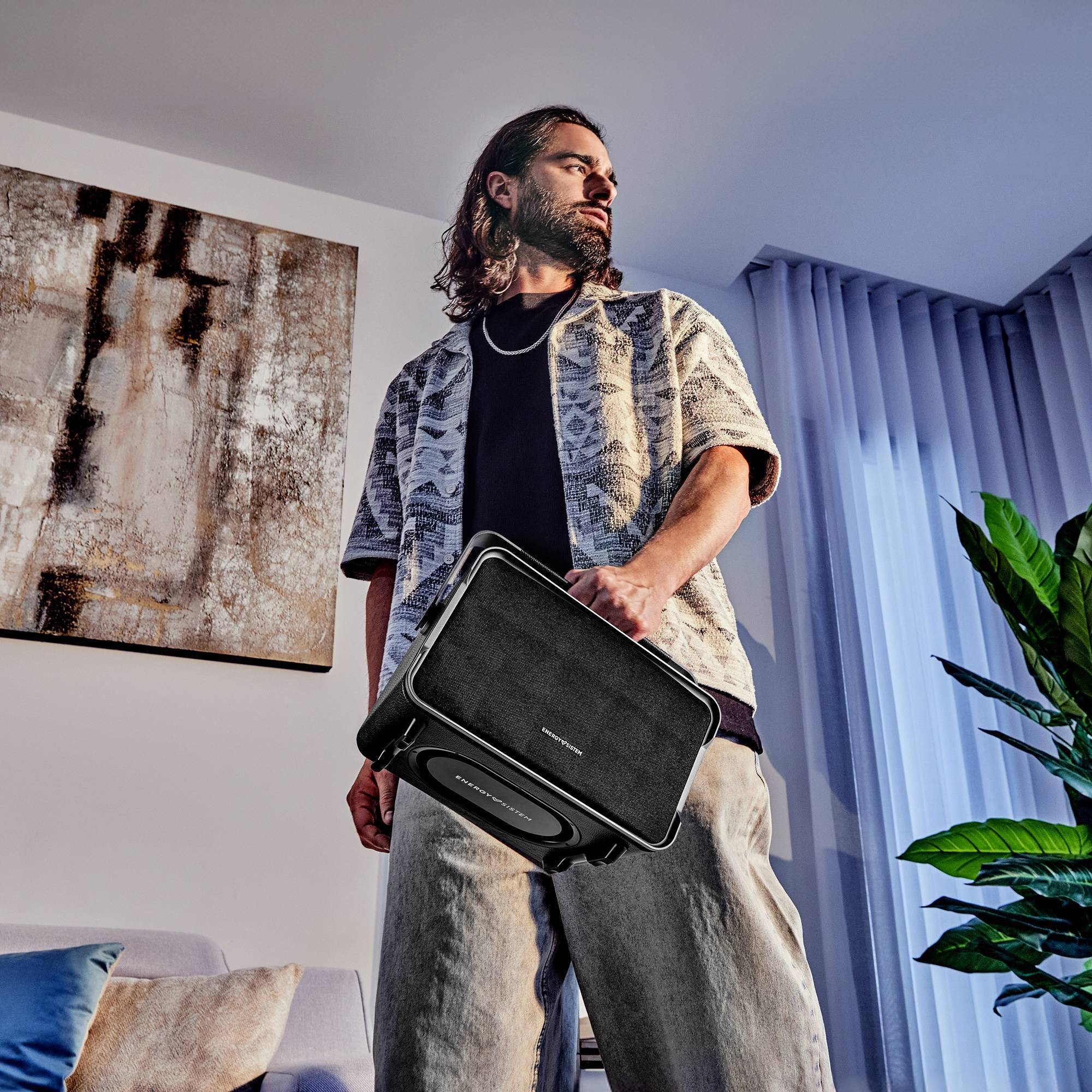 Uomo con altoparlante nero, camicia e pantaloni. Dipinto e pianta sullo sfondo.
