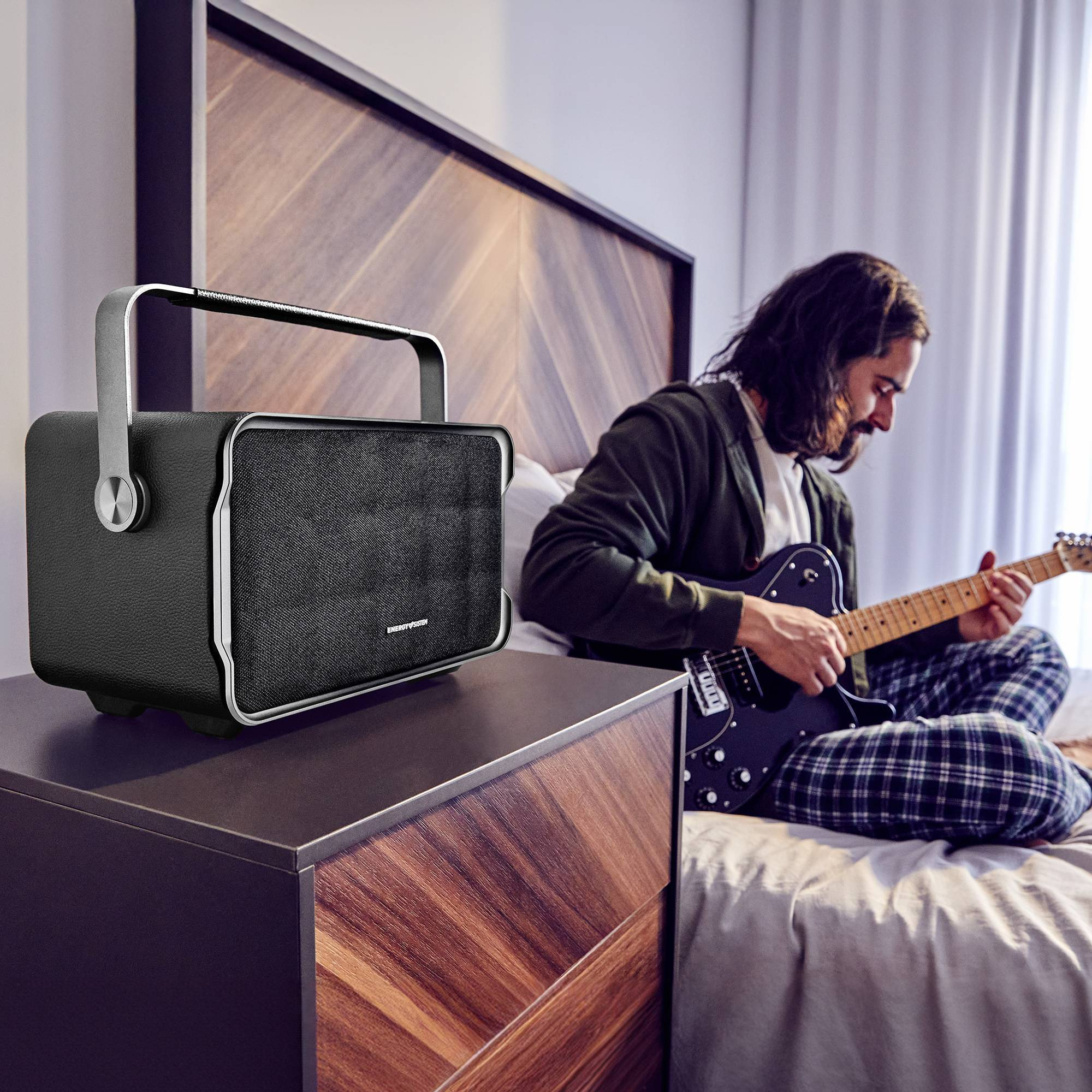 Uomo che suona la chitarra vicino a un altoparlante portatile sul comodino. Camera da letto.