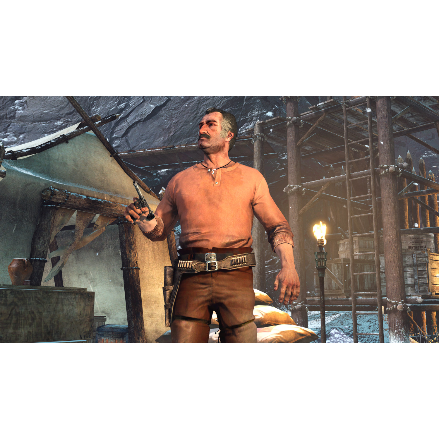A man holding a gun in a snowy environment. A wooden structure is in the background.