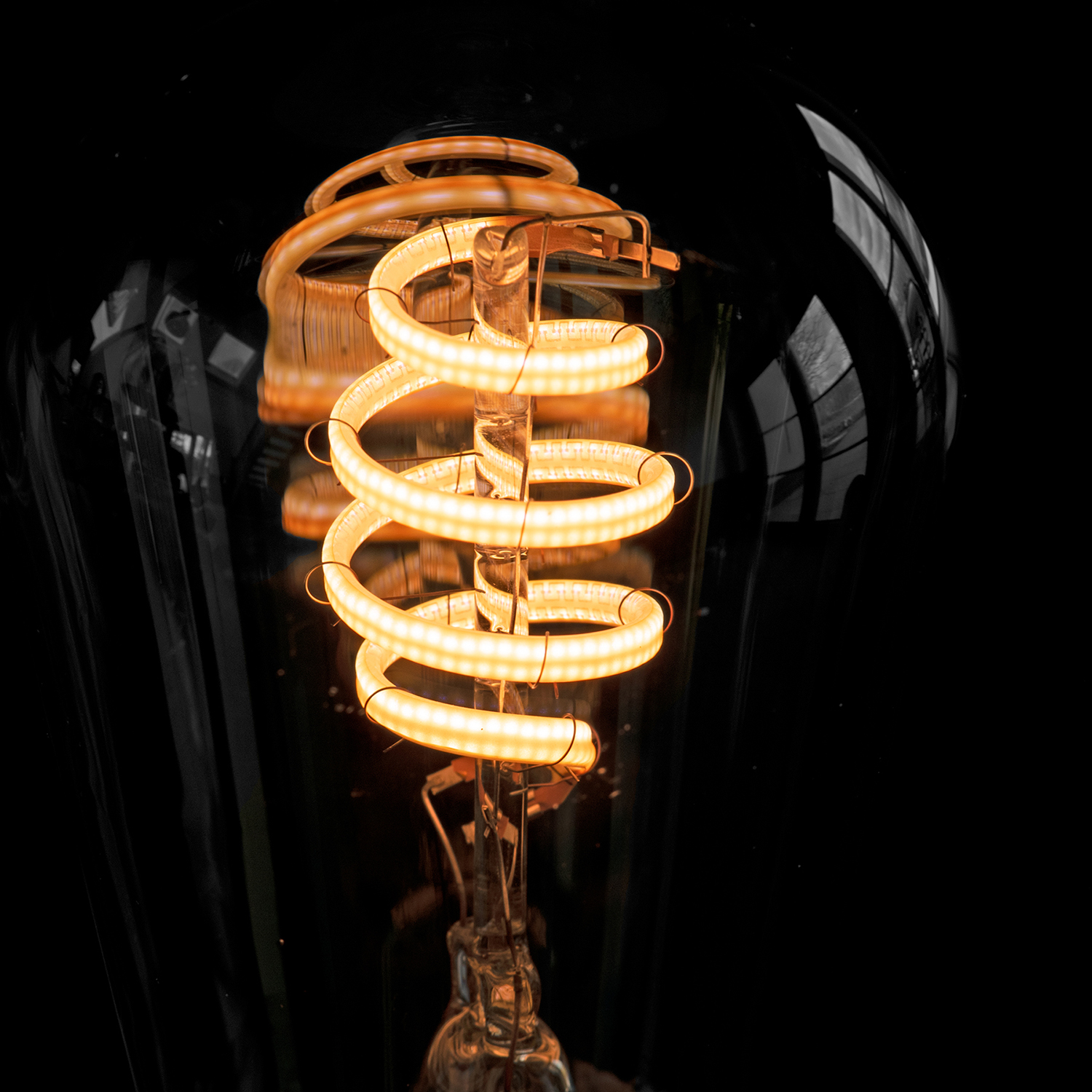 Zbliżenie żarówki ze spiralnym żarnikiem, świecącej na pomarańczowo na czarnym tle.