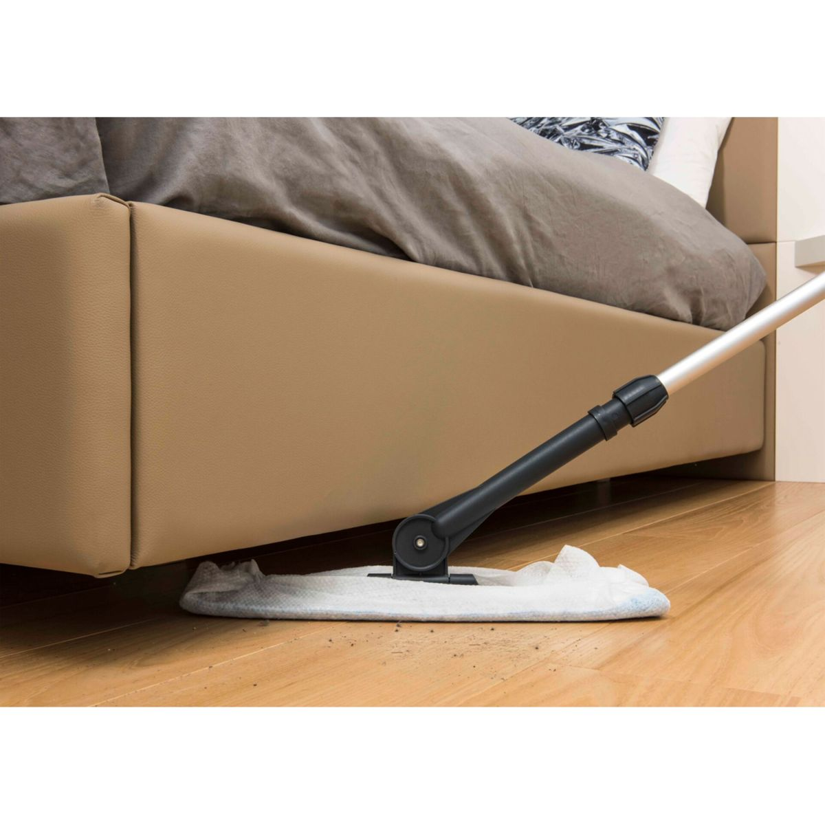 Mop czyszczący podłogę pod łóżkiem. Łóżko jest brązowe, a podłoga drewniana.