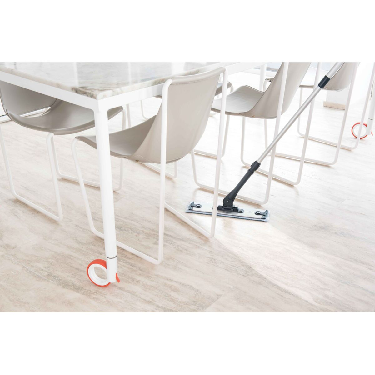 Mop na jasnej drewnianej podłodze, w pobliżu stołów i krzeseł. Białe tło.