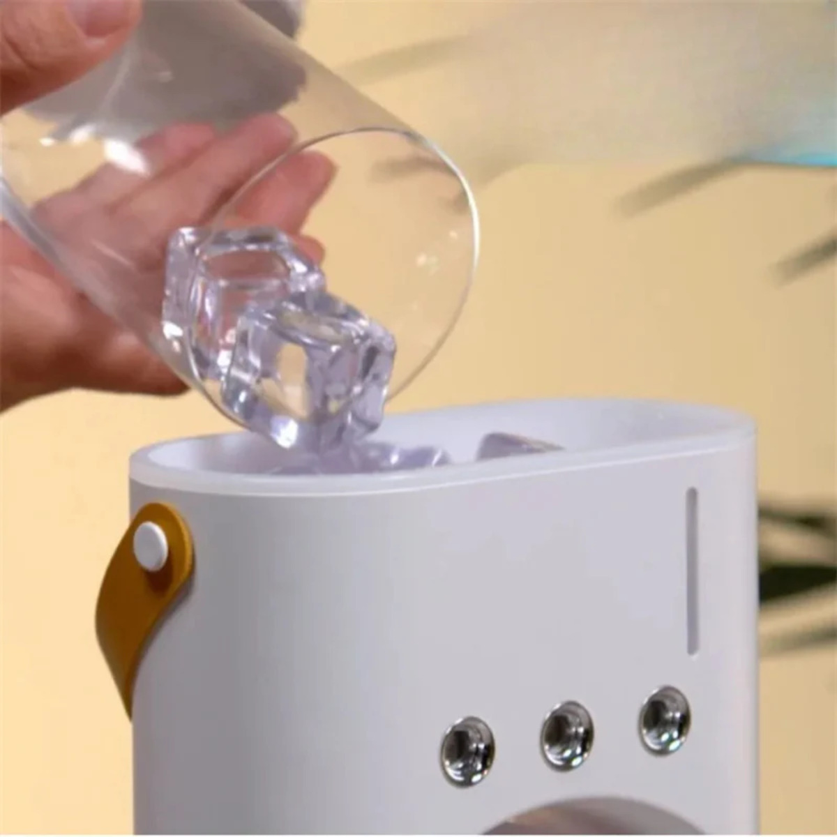 Mano vertiendo cubitos de hielo en un recipiente blanco. Asa amarilla lateral.