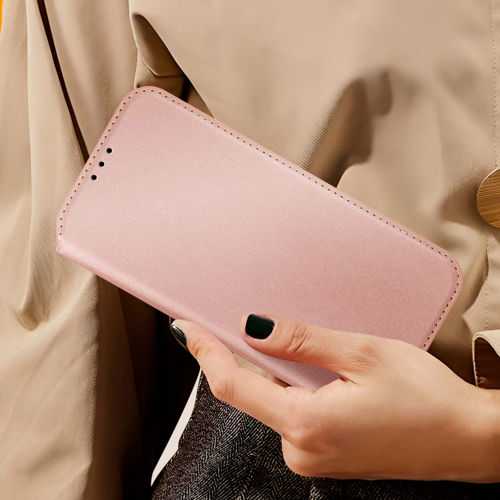 Una mano di donna che tiene una custodia rosa per telefono, primo piano, con sfondo beige.