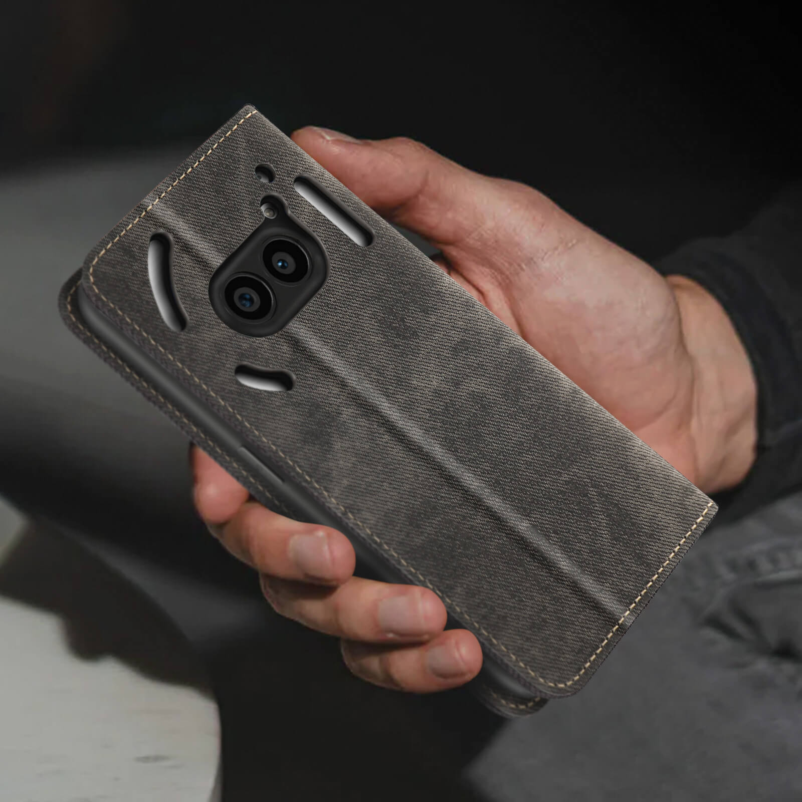 Mano che tiene una custodia grigia per telefono con un ritaglio per la fotocamera e cuciture.