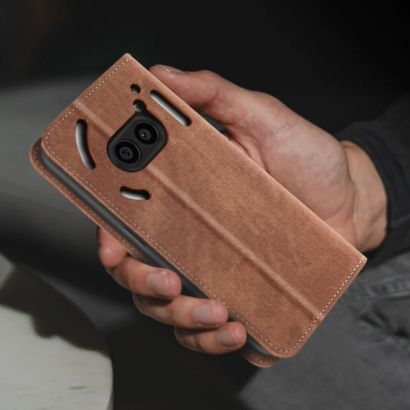 Una mano che tiene una custodia per telefono marrone. La custodia ha una superficie strutturata e ritagli per la fotocamera.
