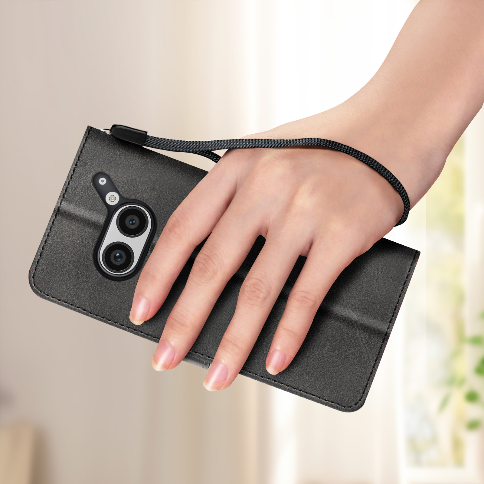 Mano che tiene una custodia nera per telefono con lenti della fotocamera e cinturino da polso.
