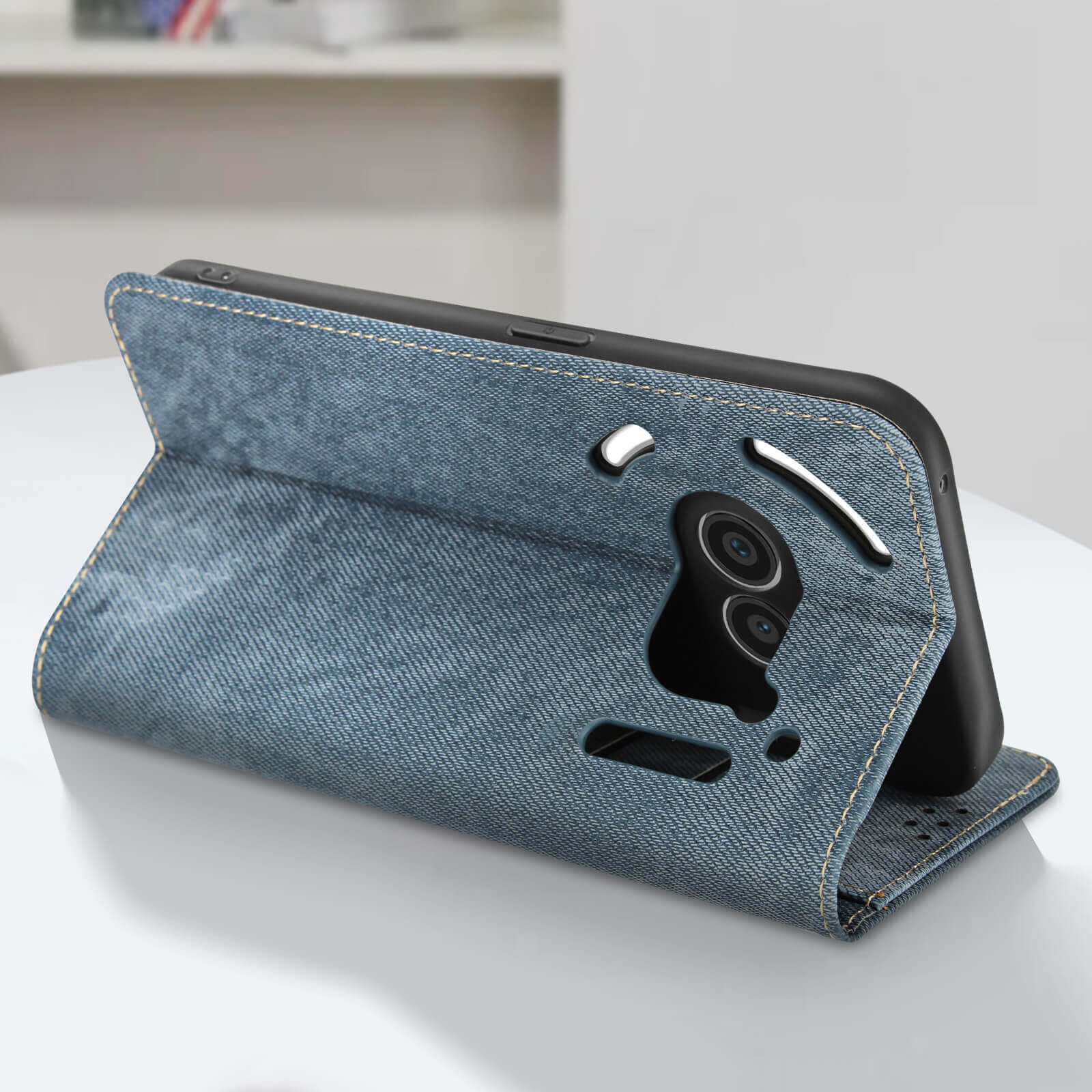Una custodia per telefono in denim è aperta. Il telefono è dentro. La custodia è su una superficie bianca.