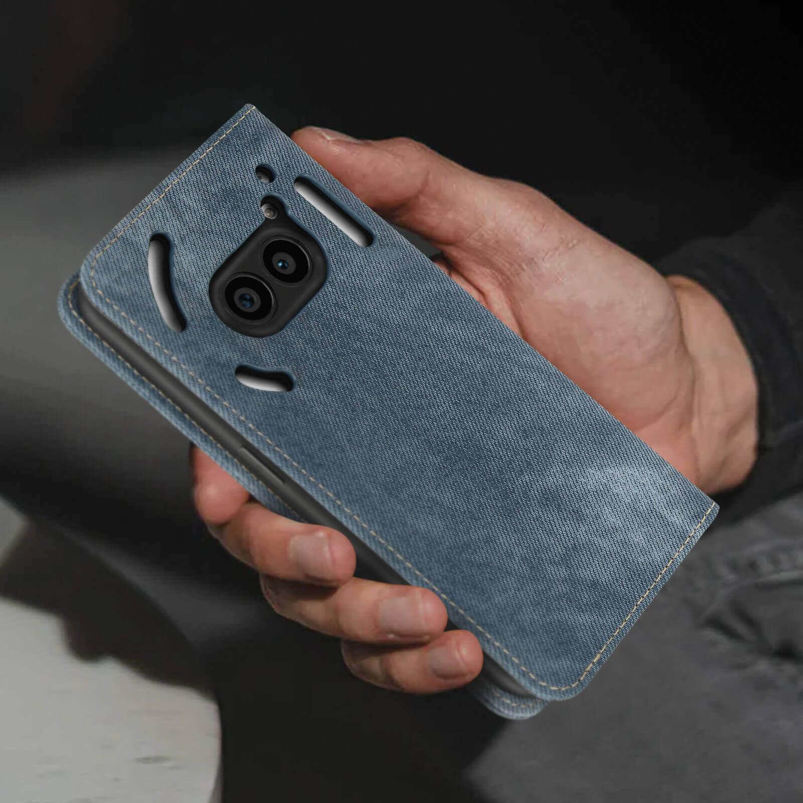 Mano che tiene una custodia per telefono in denim blu con ritaglio nero per fotocamera.
