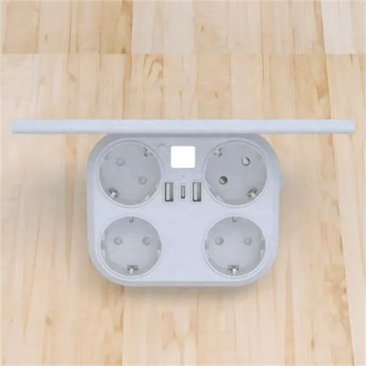 Eine weiße Steckdosenleiste mit vier Steckdosen und zwei USB-Anschlüssen befindet sich auf einer hellen Holzoberfläche.