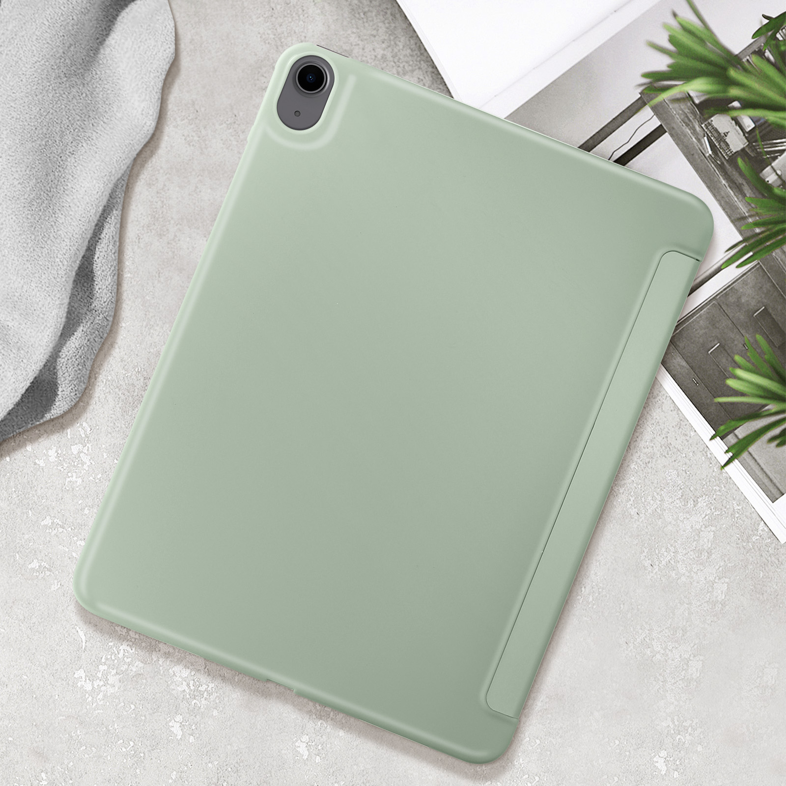 Un tablet verde chiaro con custodia su una superficie strutturata, un panno grigio e una pianta verde.