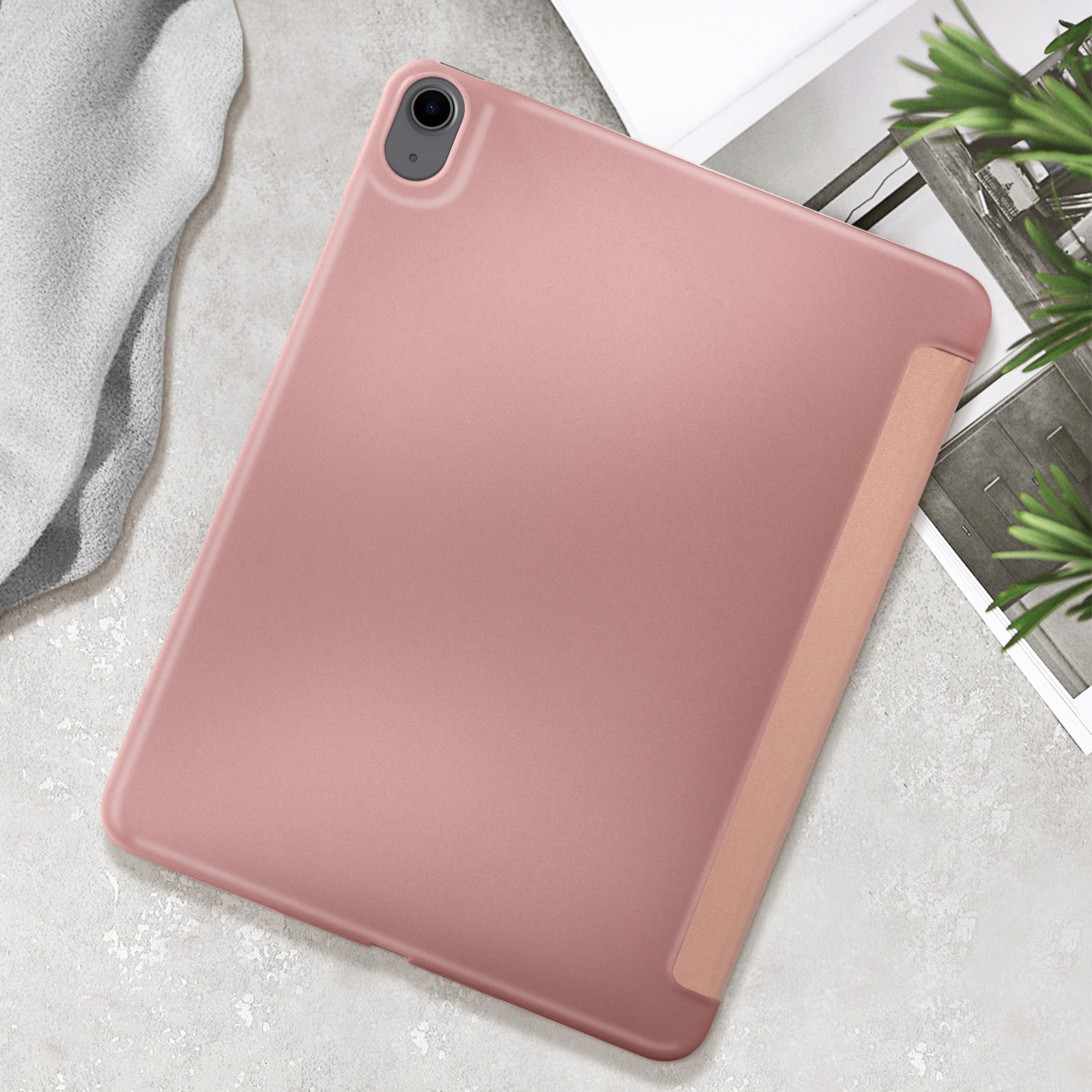 Custodia rosa per iPad. La custodia è aperta, rivelando il tablet. Lo sfondo è un tavolo e alcune foglie.