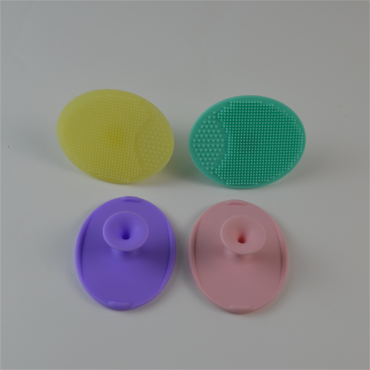 Vier farbige Silikon-Gesichtsbürsten; gelb, grün, lila, rosa.