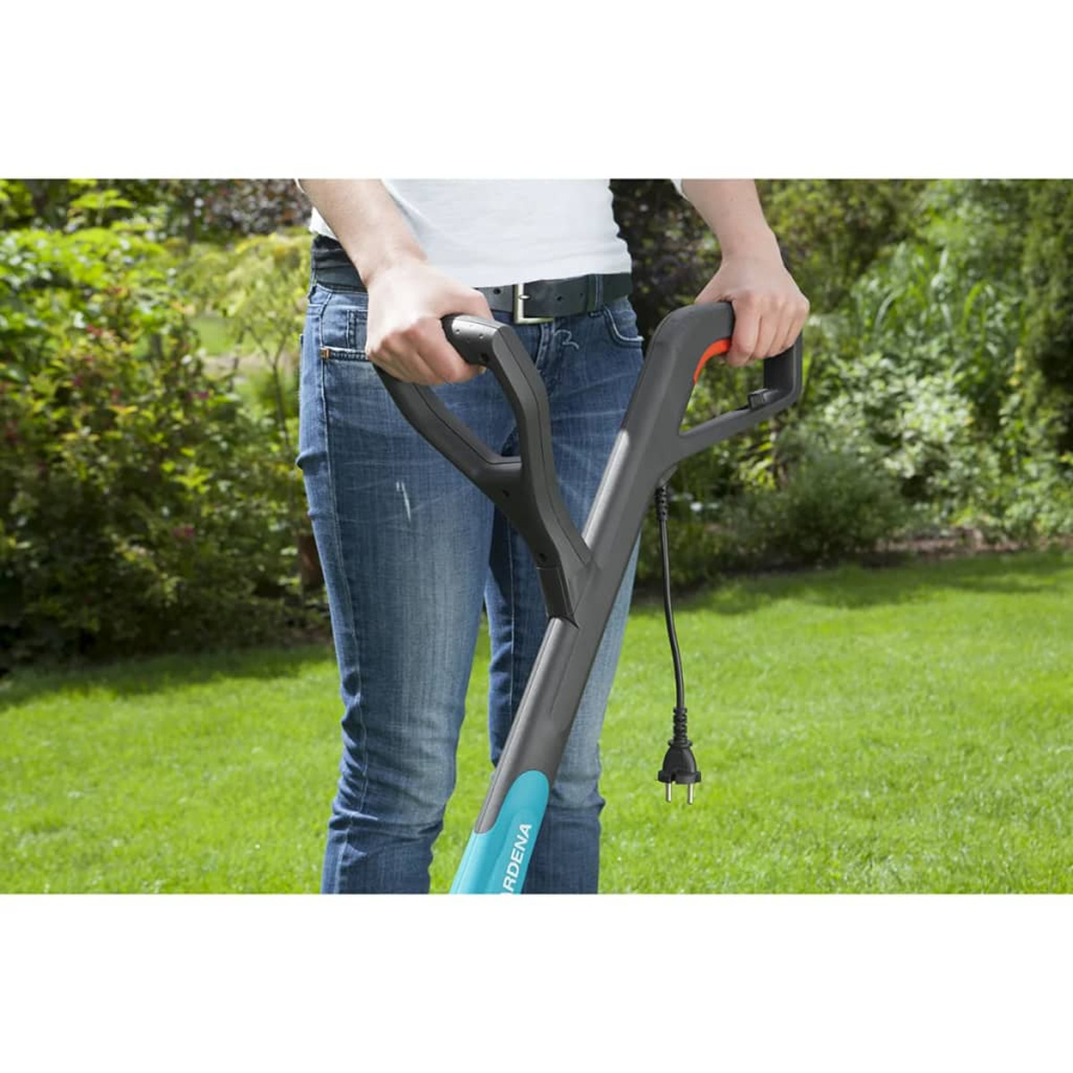 Person hält ein Gartengerät. Grünes Gras und Büsche im Hintergrund. Das Werkzeug ist schwarz und blau.