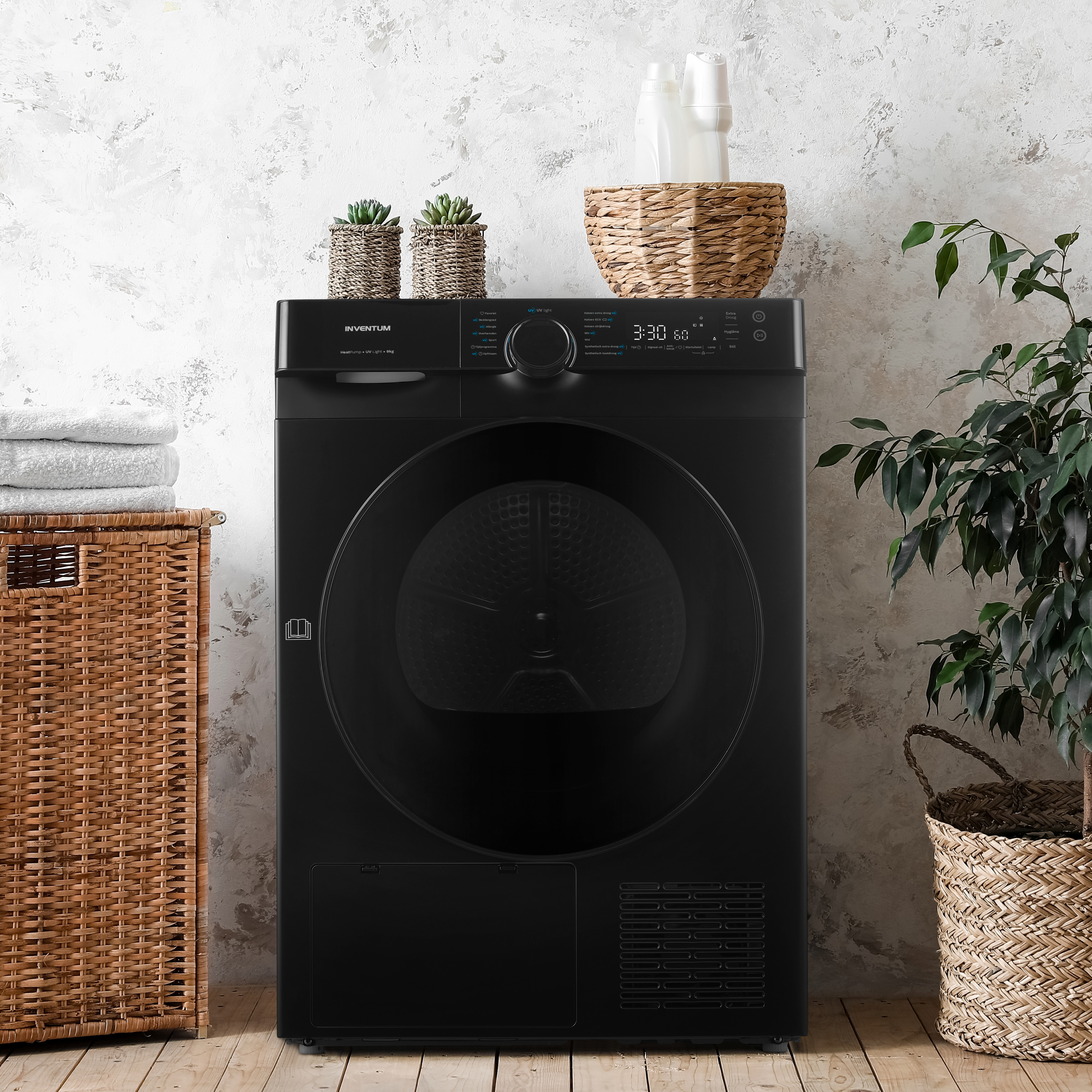 A black dryer with items on top and a plant beside it on a wooden floor.
