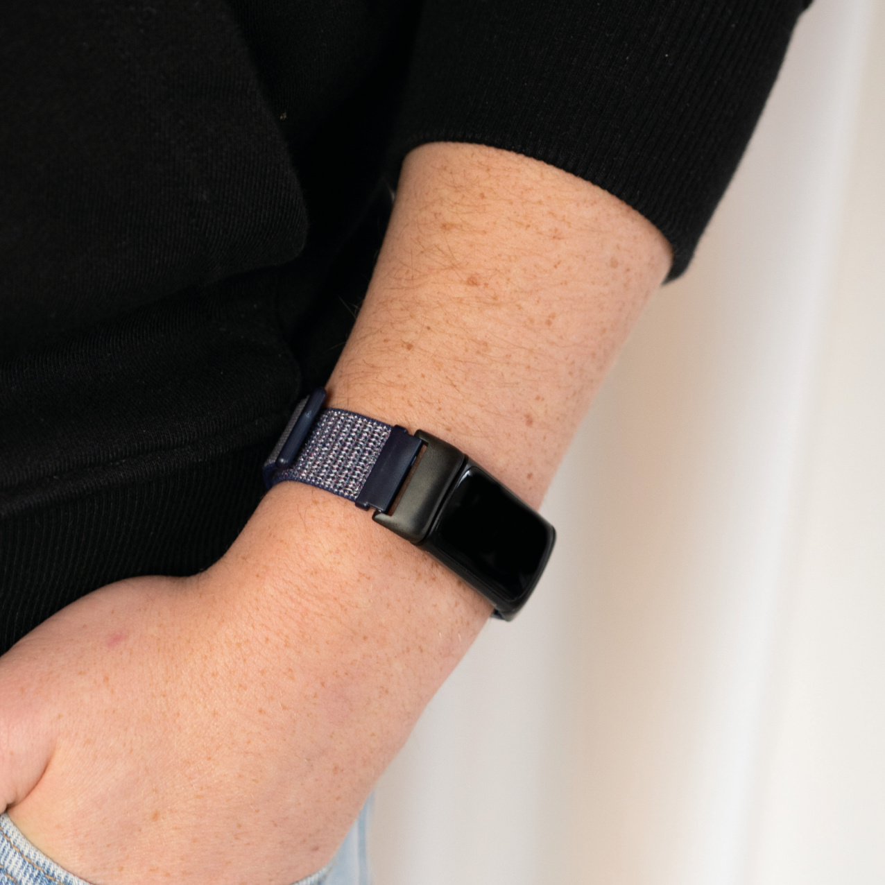 Ein Handgelenk mit einem dunkelblauen und grauen Armband. Das Band ist mit einem schwarzen Gerät verbunden.
