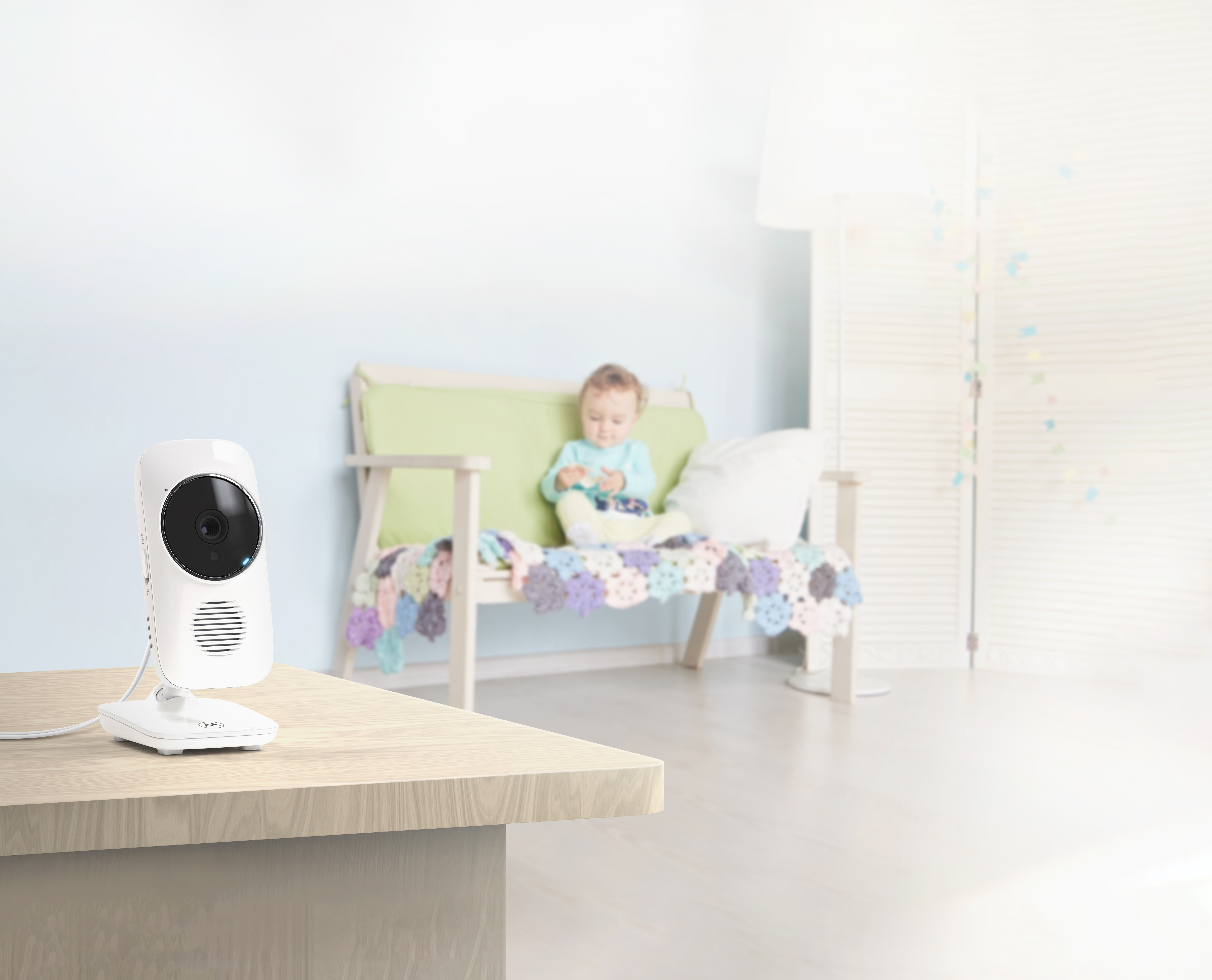 Un baby monitor su un tavolo, focalizzato sul monitor. Un bambino è sullo sfondo.