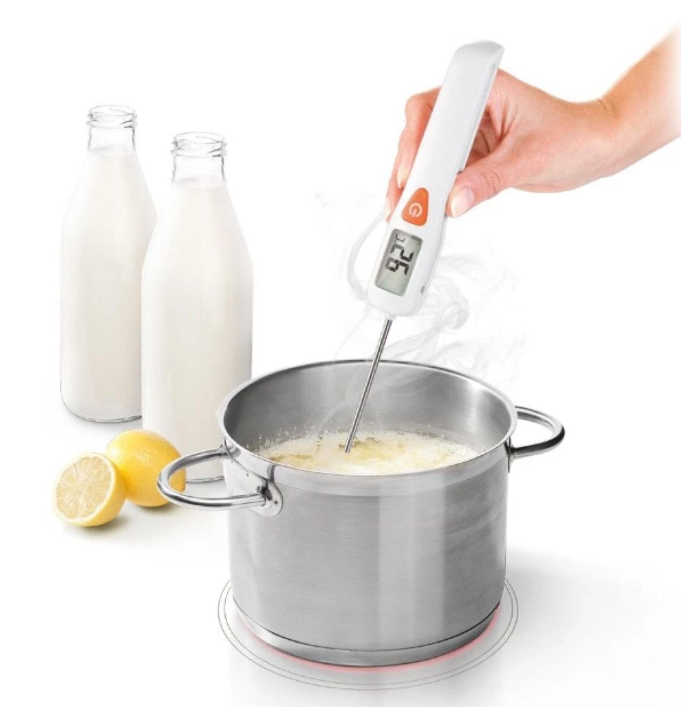 Person misst mit Thermometer die Temperatur von Kochflüssigkeit. Zwei Milchflaschen und zwei Zitronen sind vorhanden.