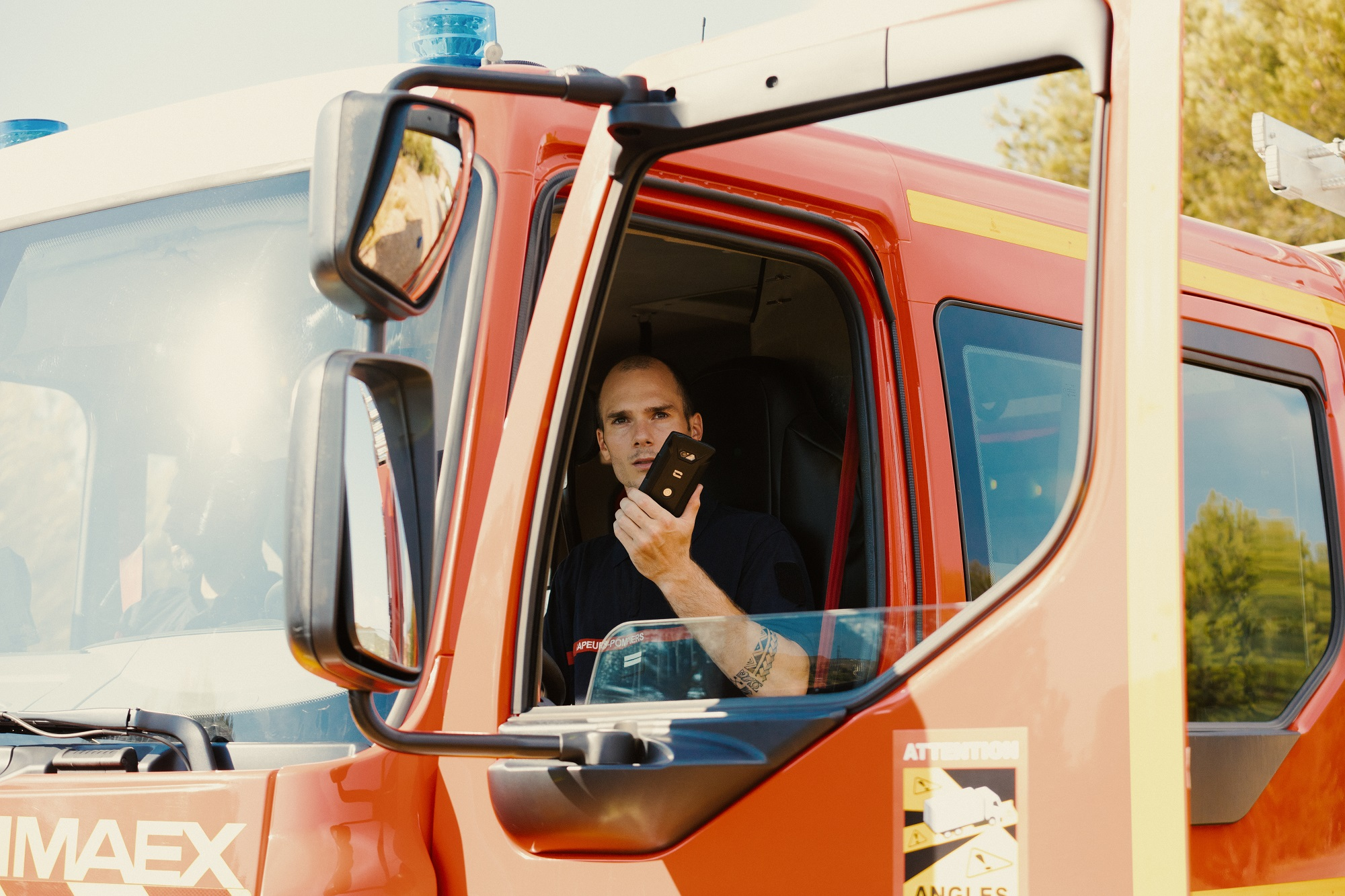 Feuerwehrmann in einem roten Feuerwehrauto. Er hält ein Gerät und schaut in die Kamera.