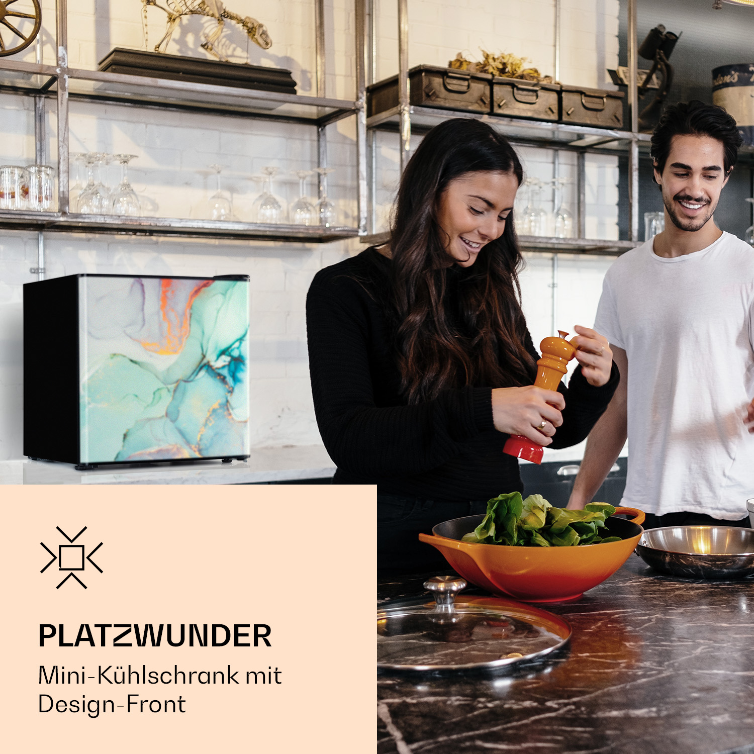 Ein Paar in einer Küche mit einem Mini-Kühlschrank, eine Person mahlt Pfeffer.
