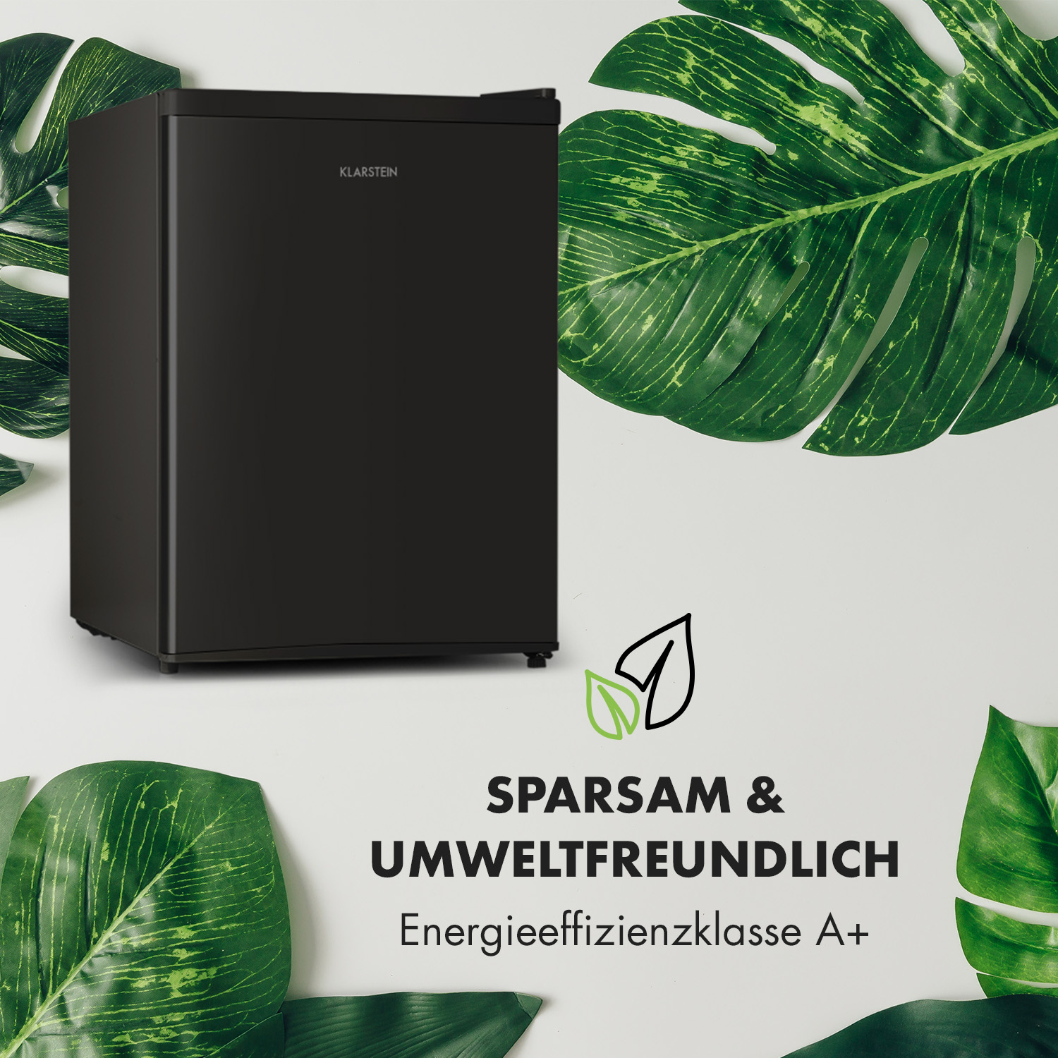 Mini-nevera negra con el texto: SPARSAM & UMWELTFREUNDLICH. Hojas verdes rodean la nevera.