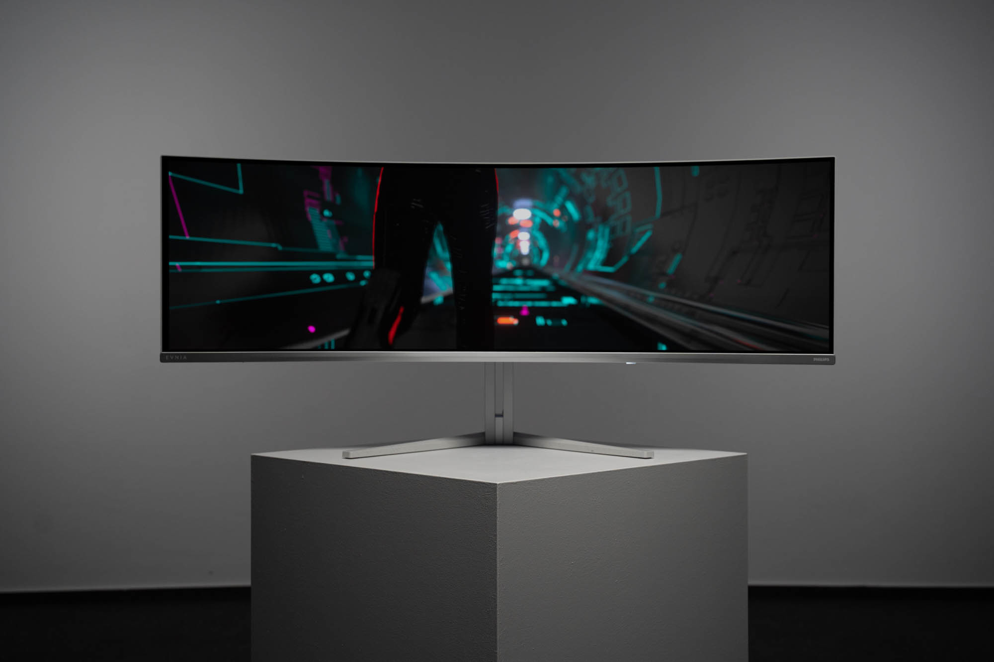 Monitor curvo su un piedistallo bianco, che mostra una scena futuristica. Sfondo grigio.