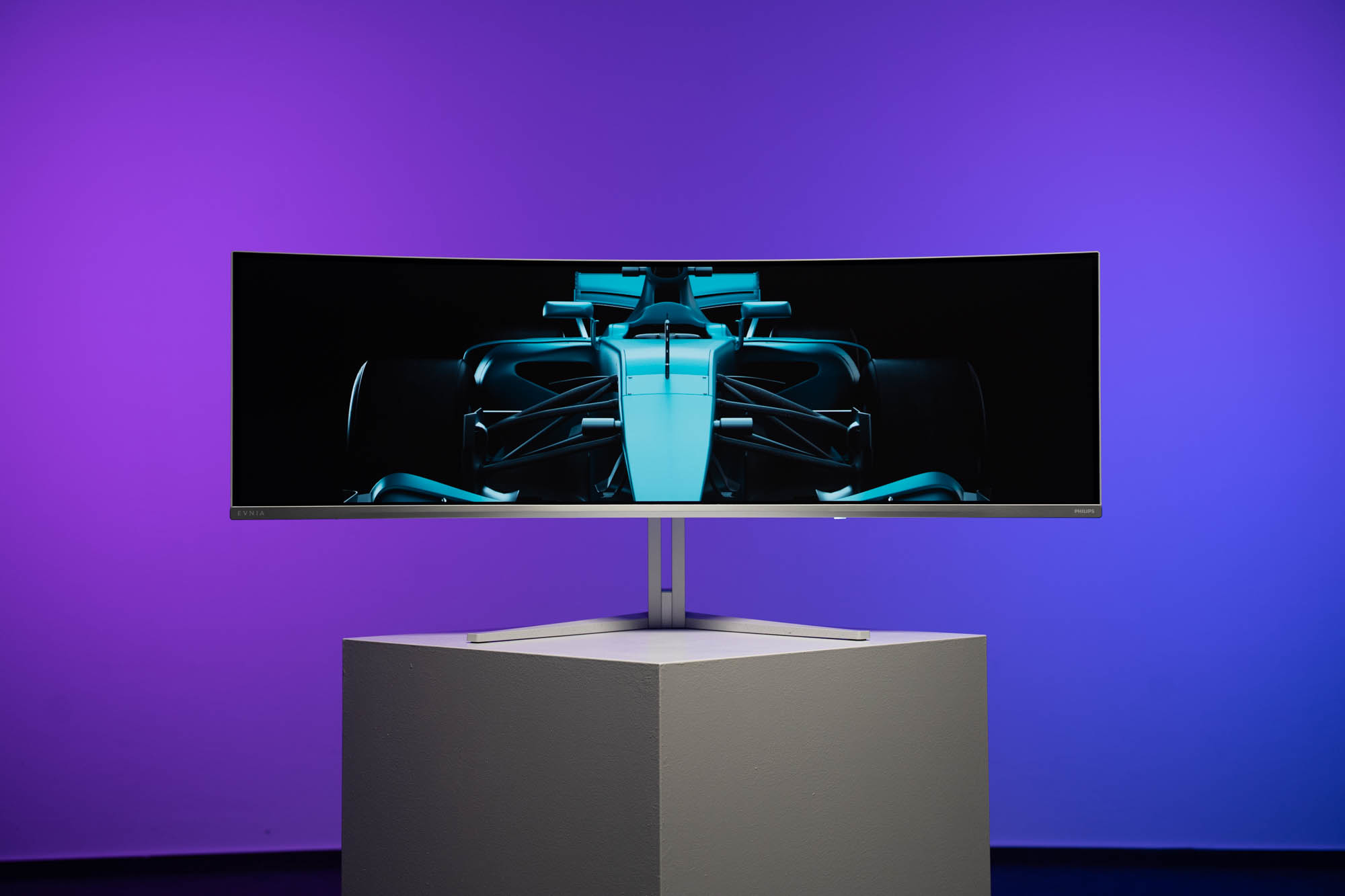 Un monitor curvo mostra un'immagine di auto da corsa blu, con sfondo viola e blu.