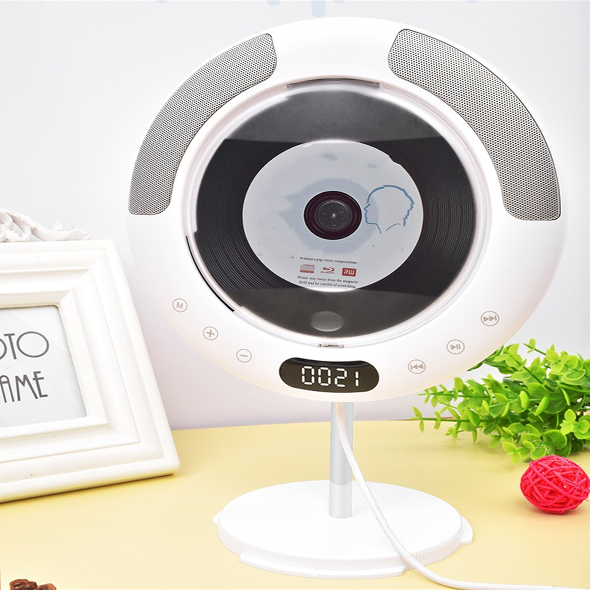 Ein weißer CD-Player mit einer CD darin. Er steht auf einem Ständer, mit einem roten Ball und einem Bilderrahmen in der Nähe.