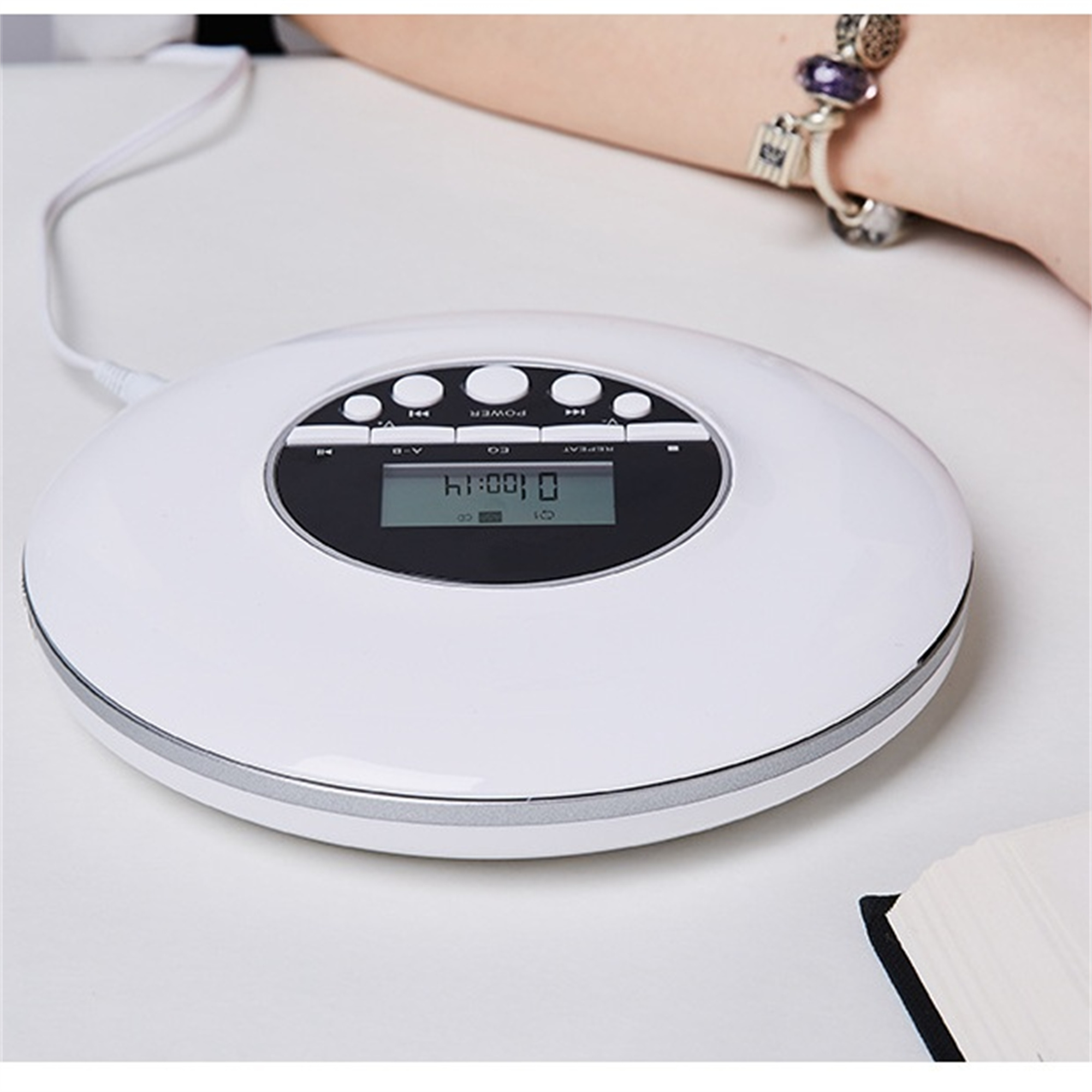 Ein weißer tragbarer CD-Player mit Knöpfen und einem kleinen Display. Ein Handgelenk im Hintergrund.
