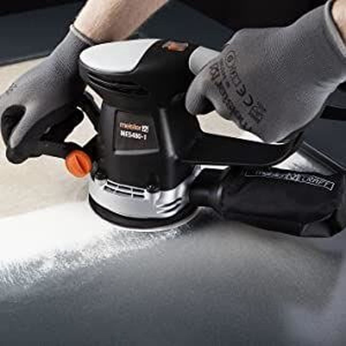 Eine Schleifmaschine wird von einer Person mit grauen Handschuhen benutzt. Die Maschine ist schwarz und weiß.