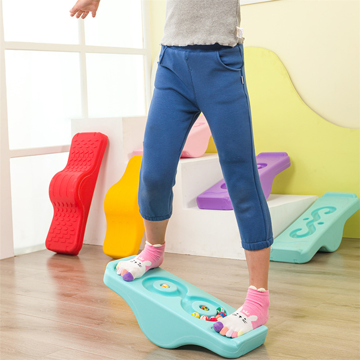 Ein Kind steht auf einem türkisfarbenen Balance Board, andere Balancierspielzeuge im Hintergrund.