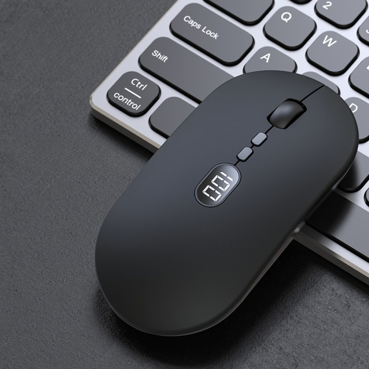 Eine schwarze kabellose Maus auf einer Tastatur. Die Maus hat eine kleine Anzeige mit 100.