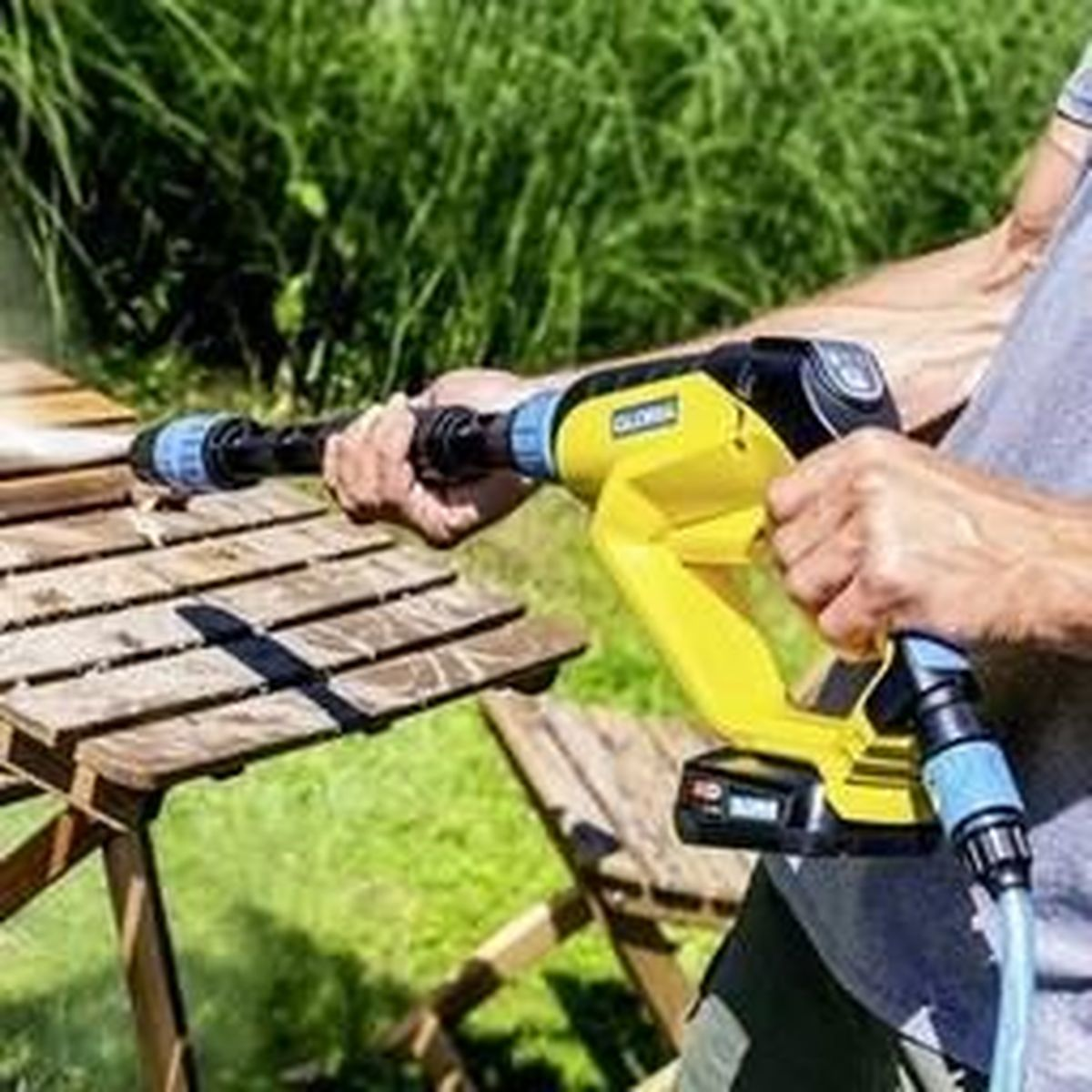 Una persona usa un'idropulitrice giallo e nera su una superficie di legno all'aperto, spruzzando acqua.