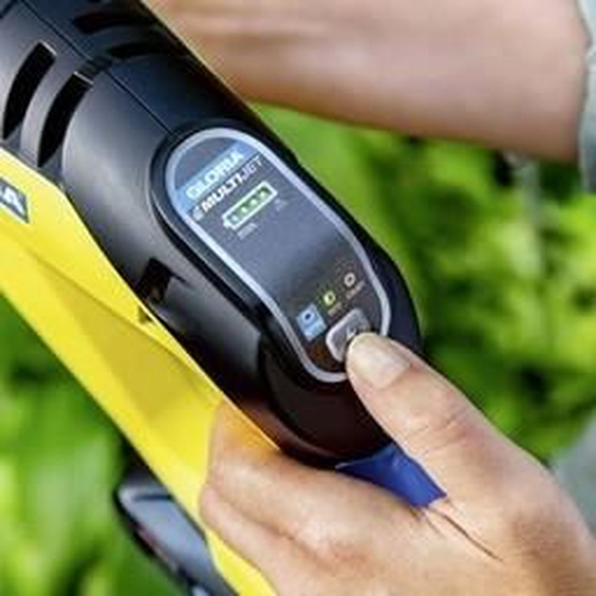 La mano di una persona preme un pulsante su un attrezzo da giardinaggio nero e giallo.