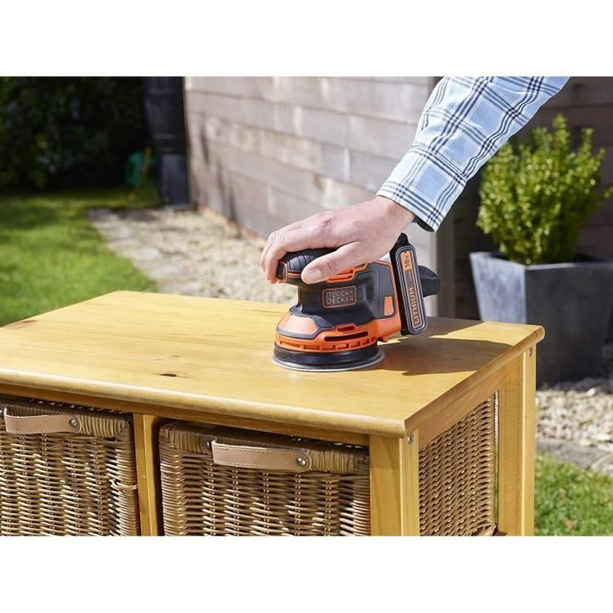 Une personne ponçant une armoire en bois avec une ponceuse électrique orange et noire, en extérieur.