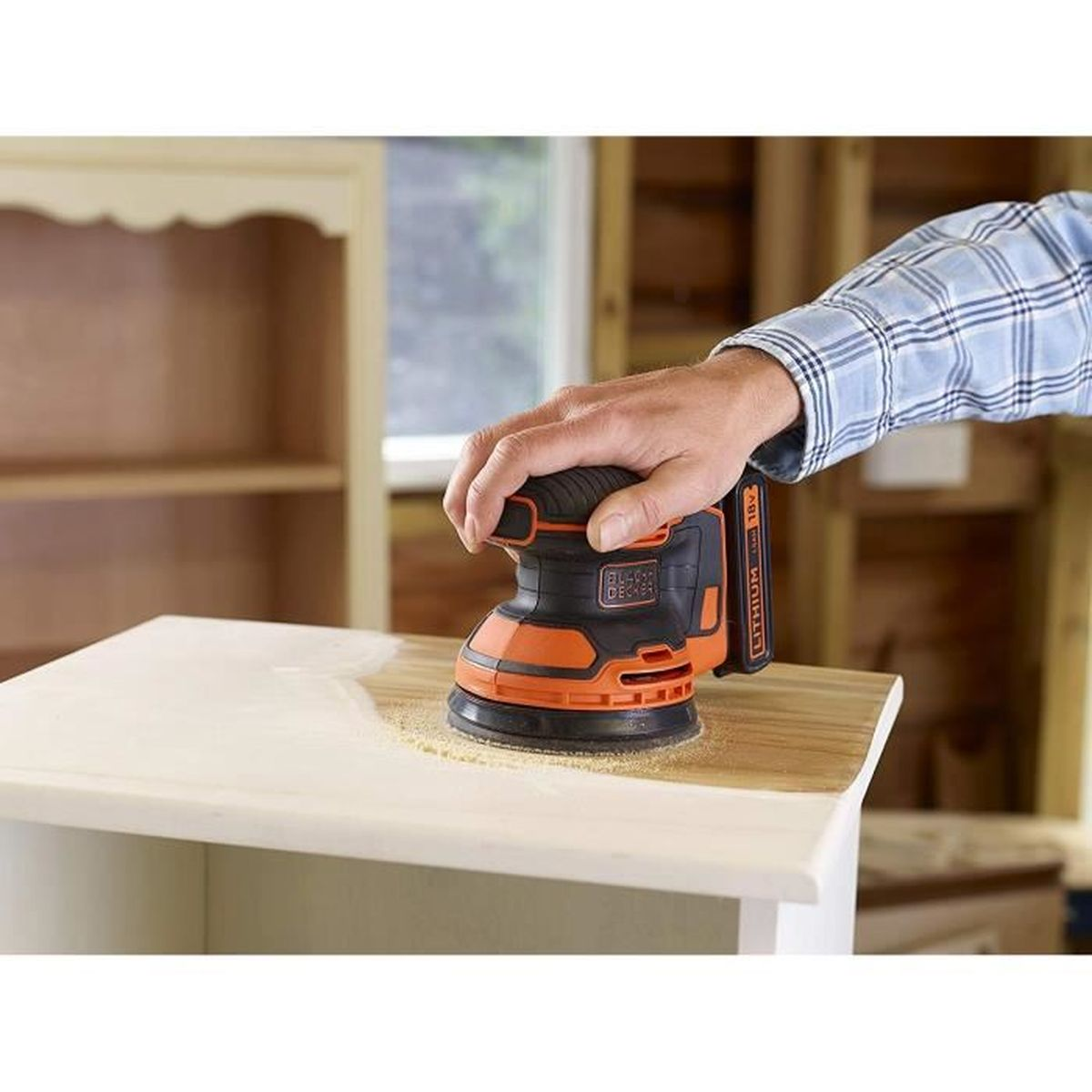 Une personne ponçant une surface en bois avec une ponceuse orange et noire.