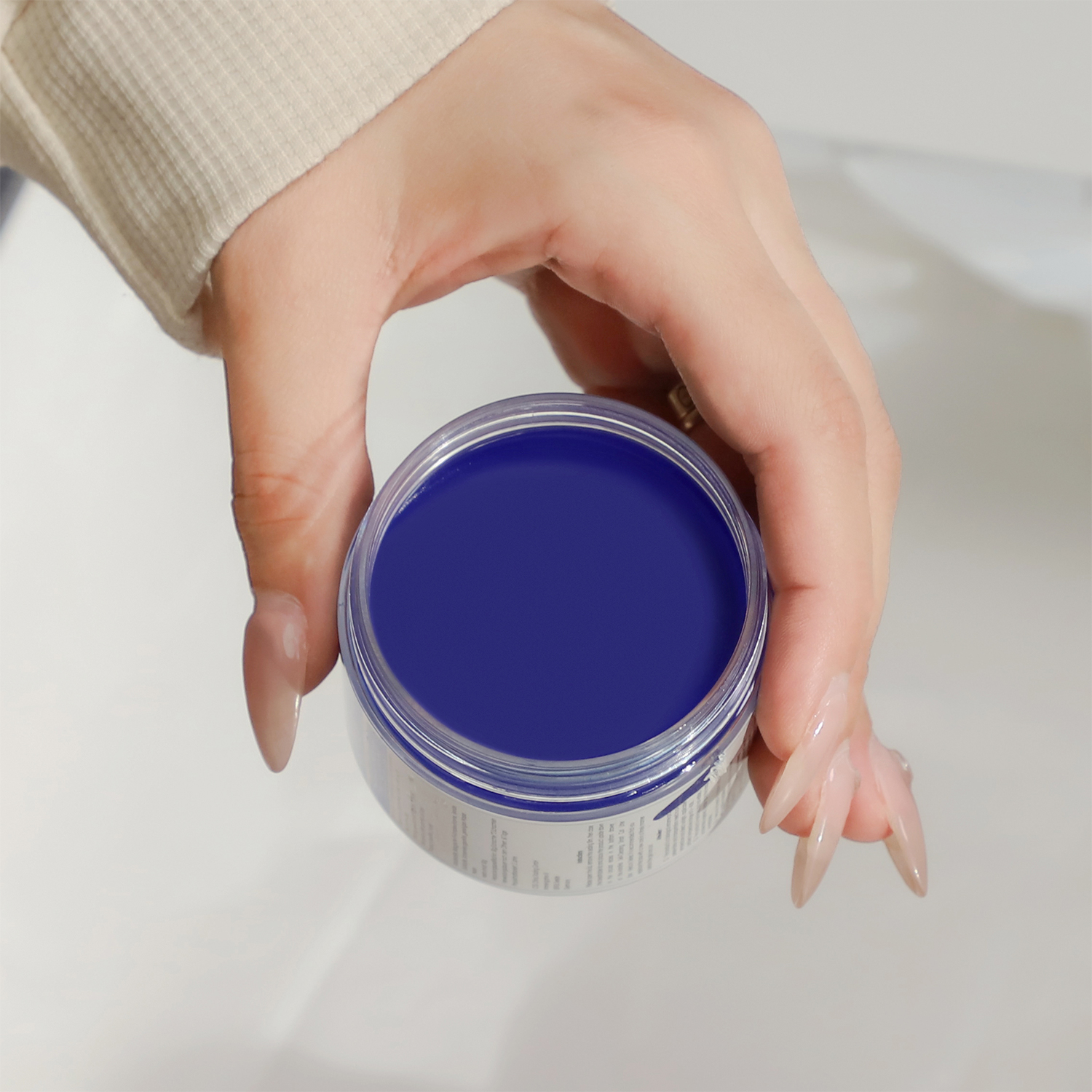 Eine Hand hält ein Glas mit blauem Nagelgel. Das Glas ist klar mit einem weißen Etikett.