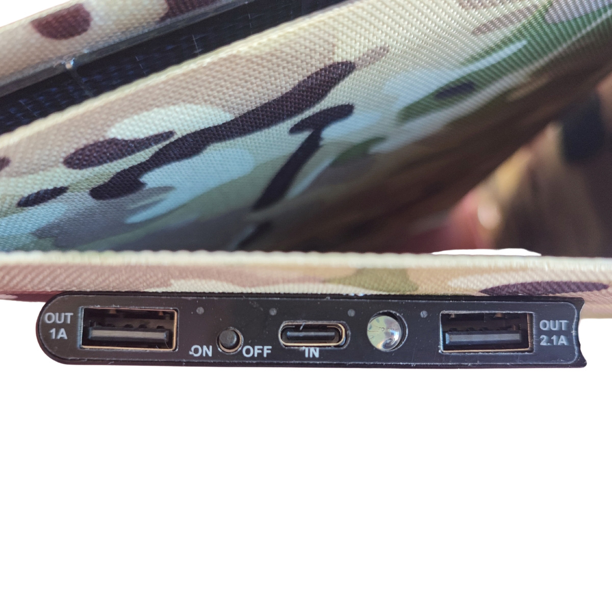 Banco de energía mostrando puertos USB y botones. Fondo con patrón de camuflaje.