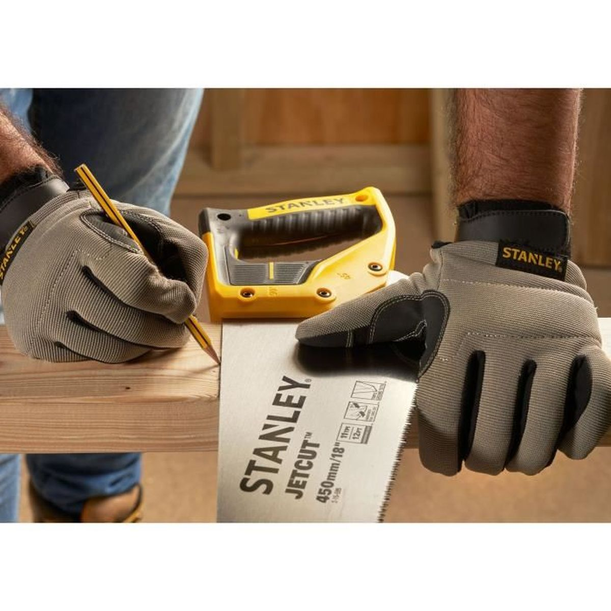 Hände in Handschuhen, eine benutzt einen Bleistift, um ein Holzbrett zu markieren. Eine Säge und ihr gelber Griff sind in der Nähe.